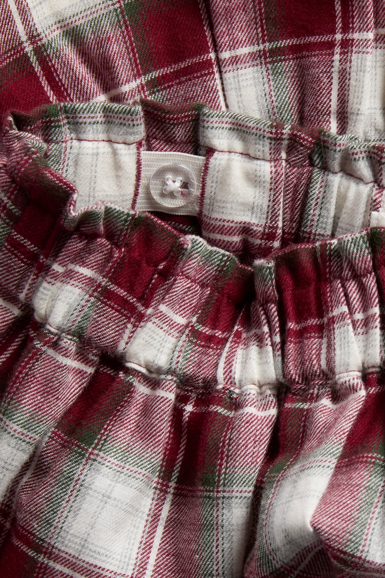 Close-up of red, white, and green plaid fabric with gathered adjustable elastic waistband and button.