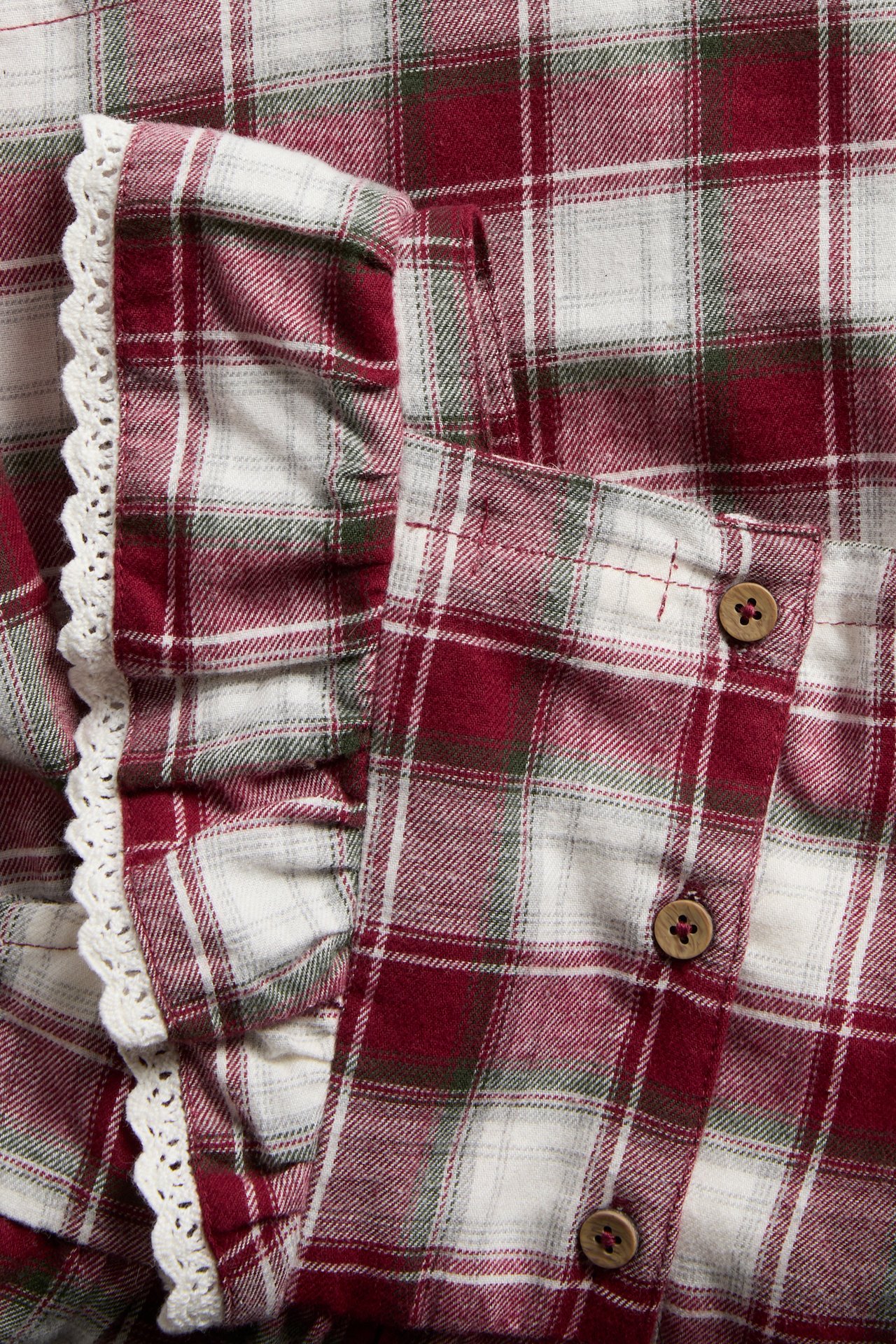 Close-up of red, white, green plaid flannel garment with ruffles, lace trim, and wood buttons.