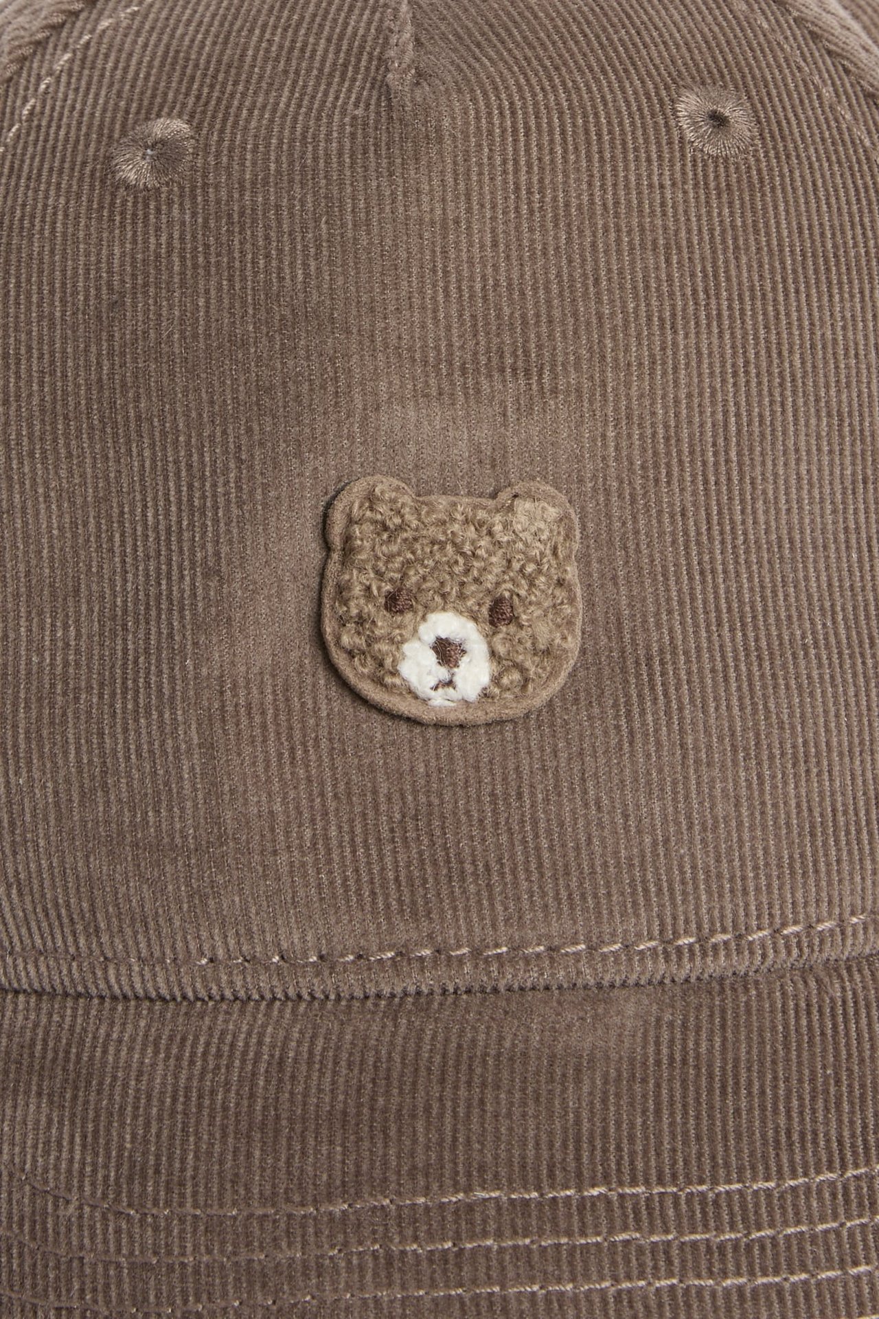 Nahaufnahme einer braunen Kordkappe mit einem gestickten Teddybär.