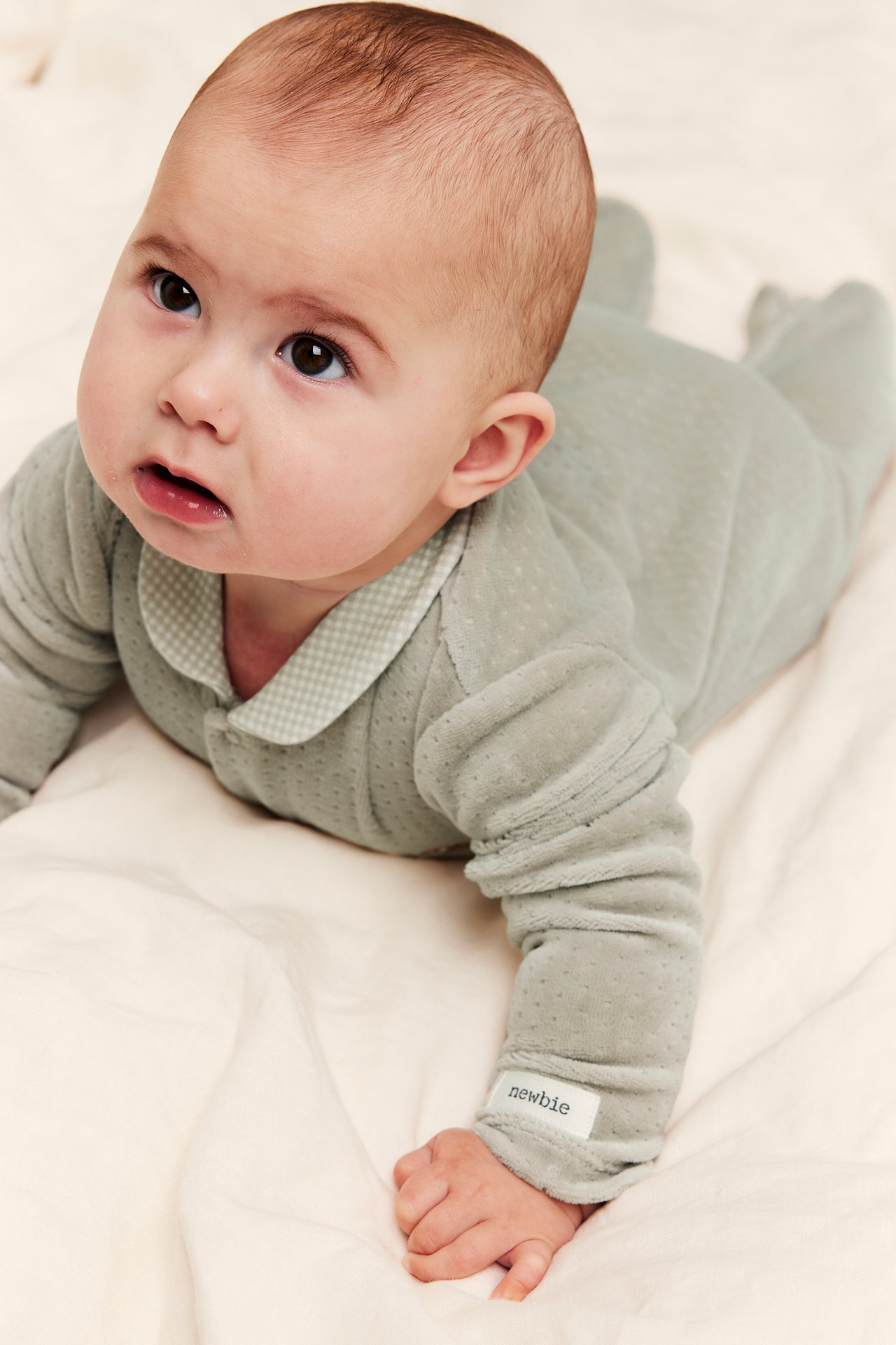 Nahaufnahme eines Babys in einem salbeigrünen gepunkteten Velours-Strampler mit Vichy-Kragen.