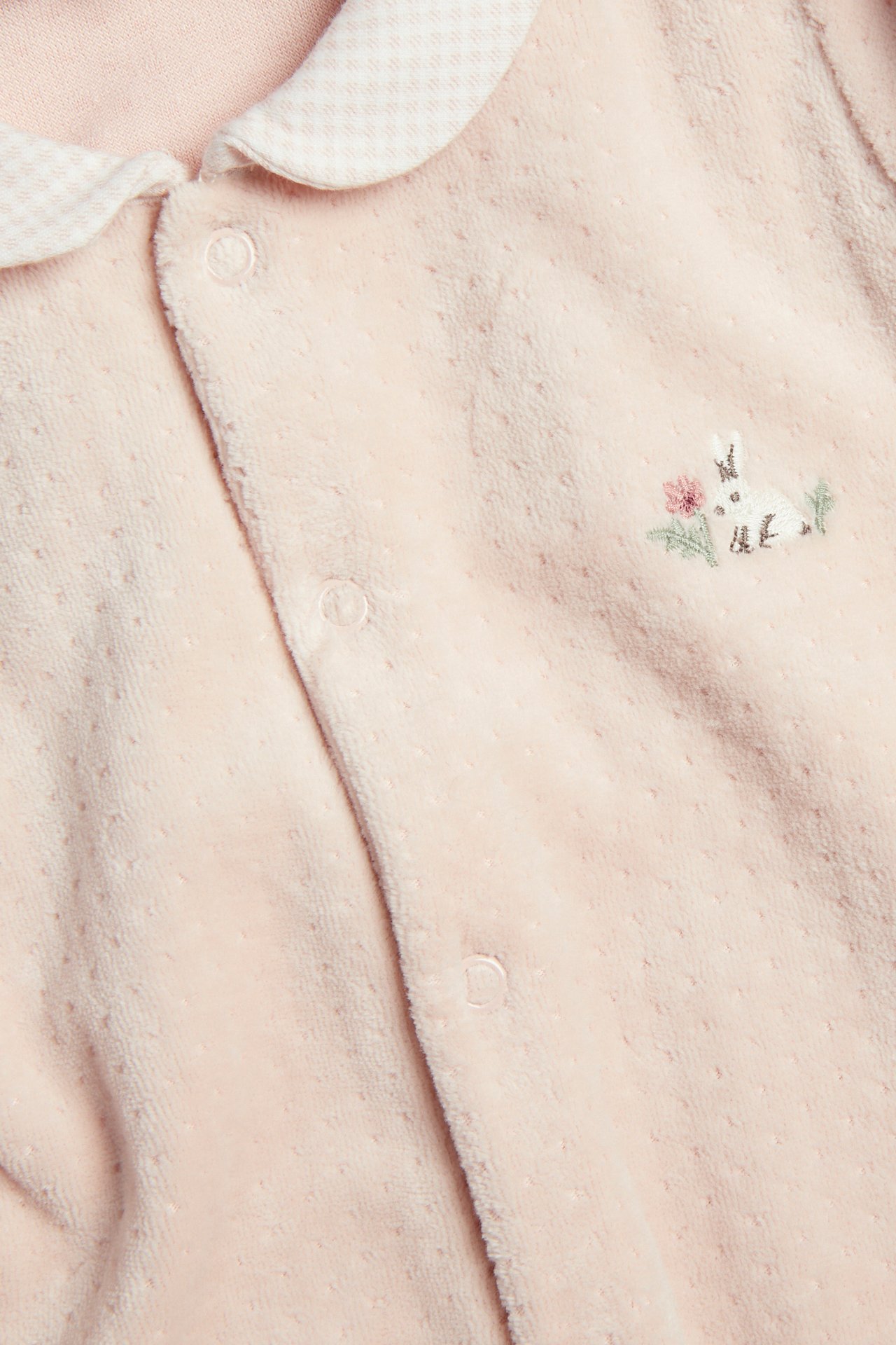 Close-up of a baby's pale pink dotted sleeper with a checkered collar and rabbit embroidery.