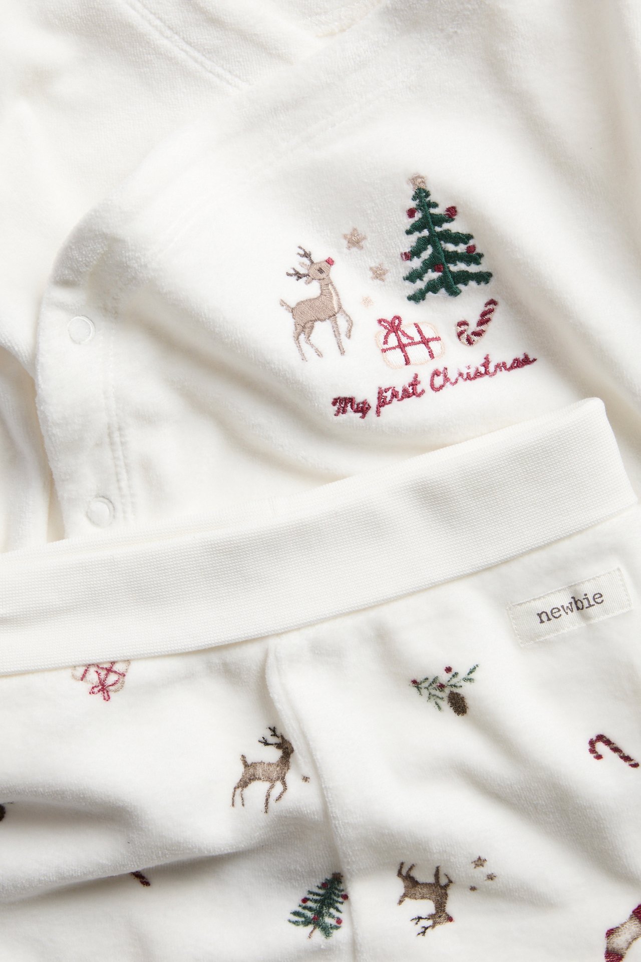 Nahaufnahme eines weichen weißen Baby-Tops mit 'My first Christmas'-Stickerei und passender Hose.
