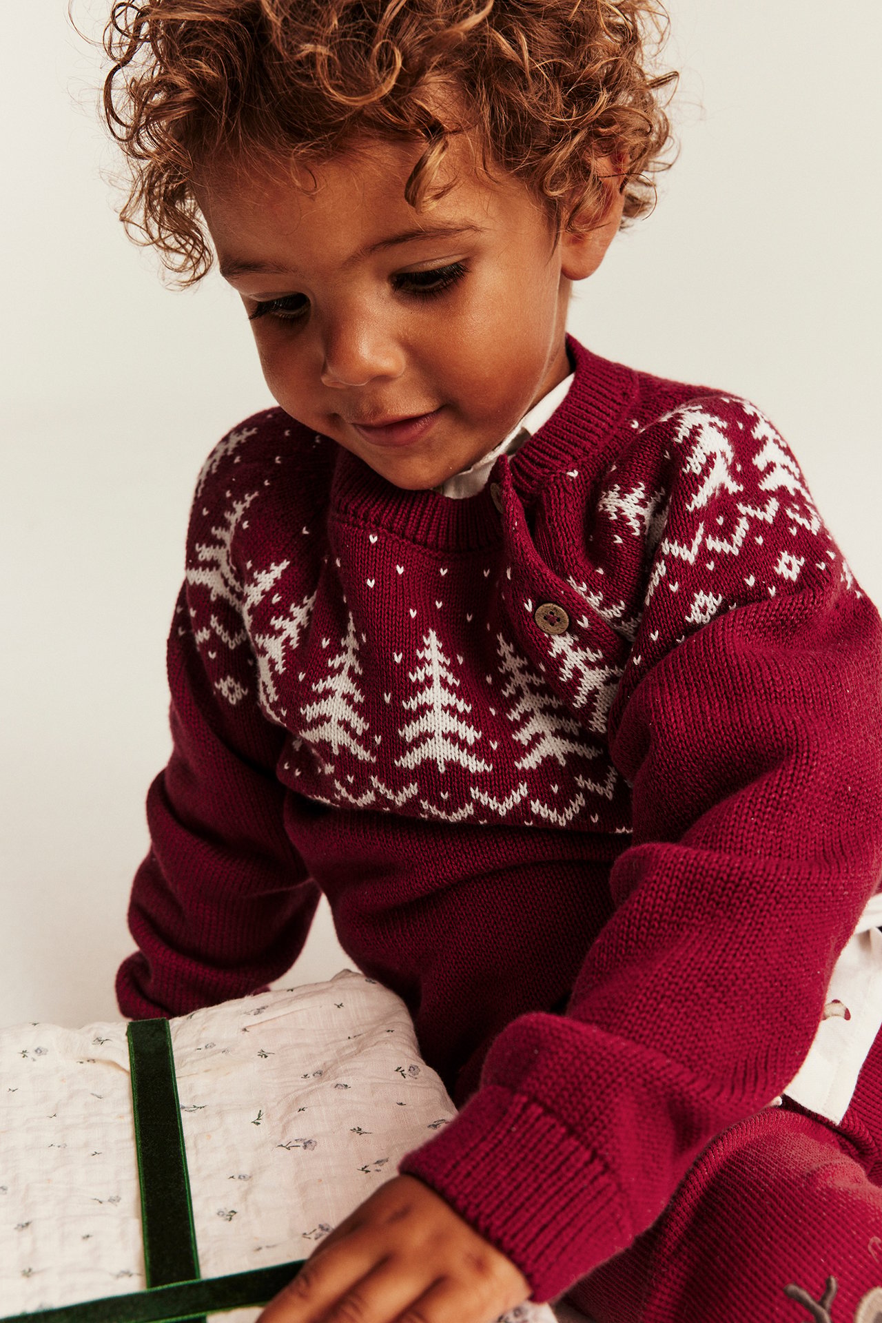 Nahaufnahme von Baby in rotem Strick-Weihnachtspullover mit weißen Mustern und passender Hose.