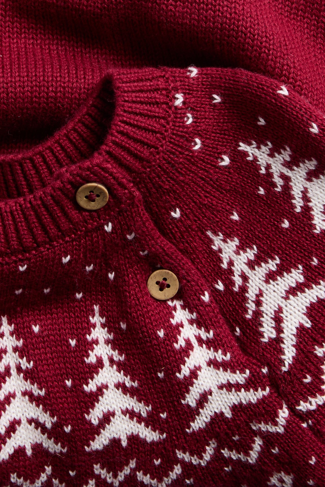 Nahaufnahme einer roten Strickjacke mit weißen Weihnachtsbäumen, Schneeflocken und Holzknöpfen.