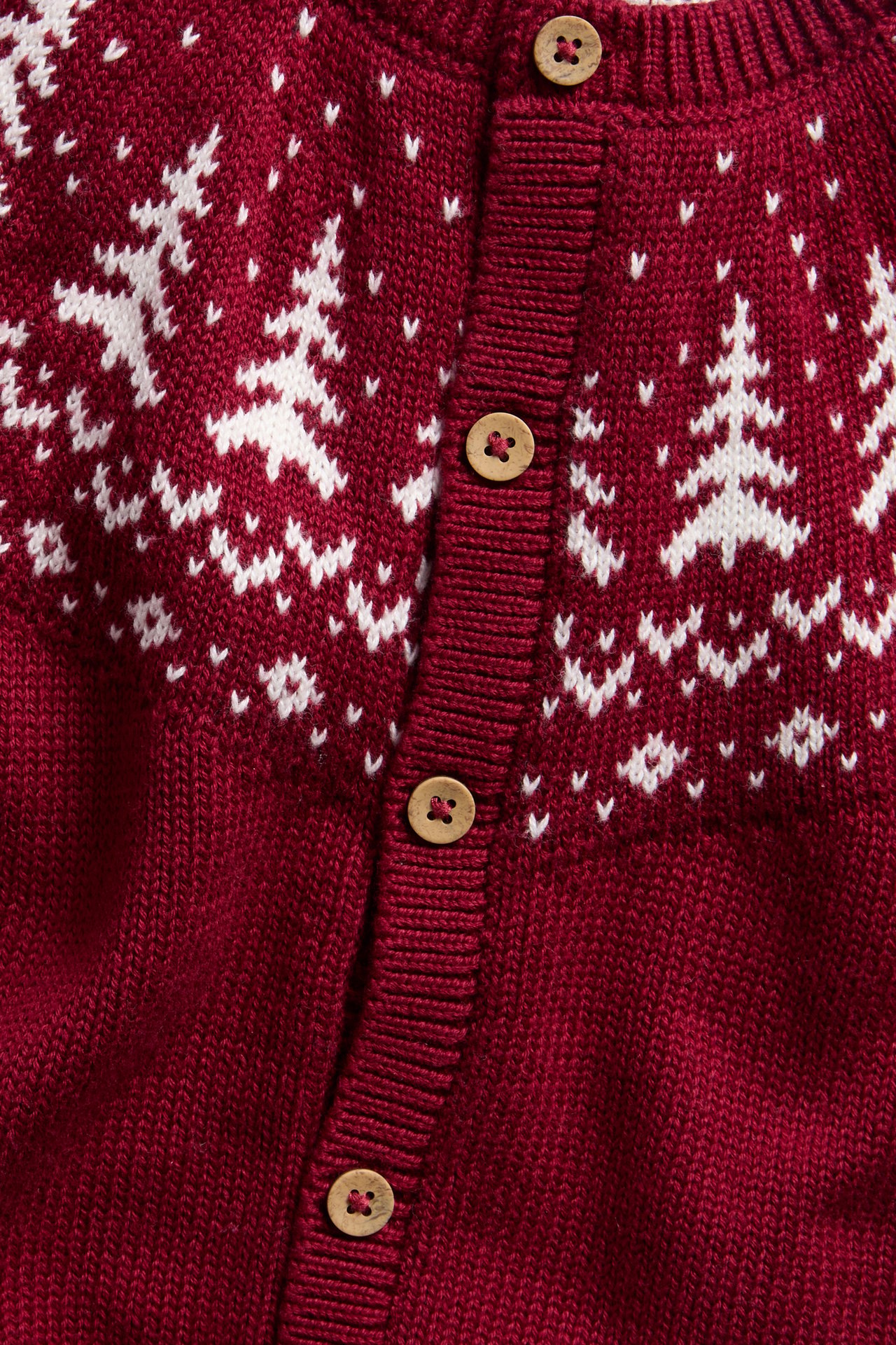 Nahaufnahme einer roten Strickjacke mit weißen Weihnachtsbäumen, Schneeflocken und Holzknöpfen.