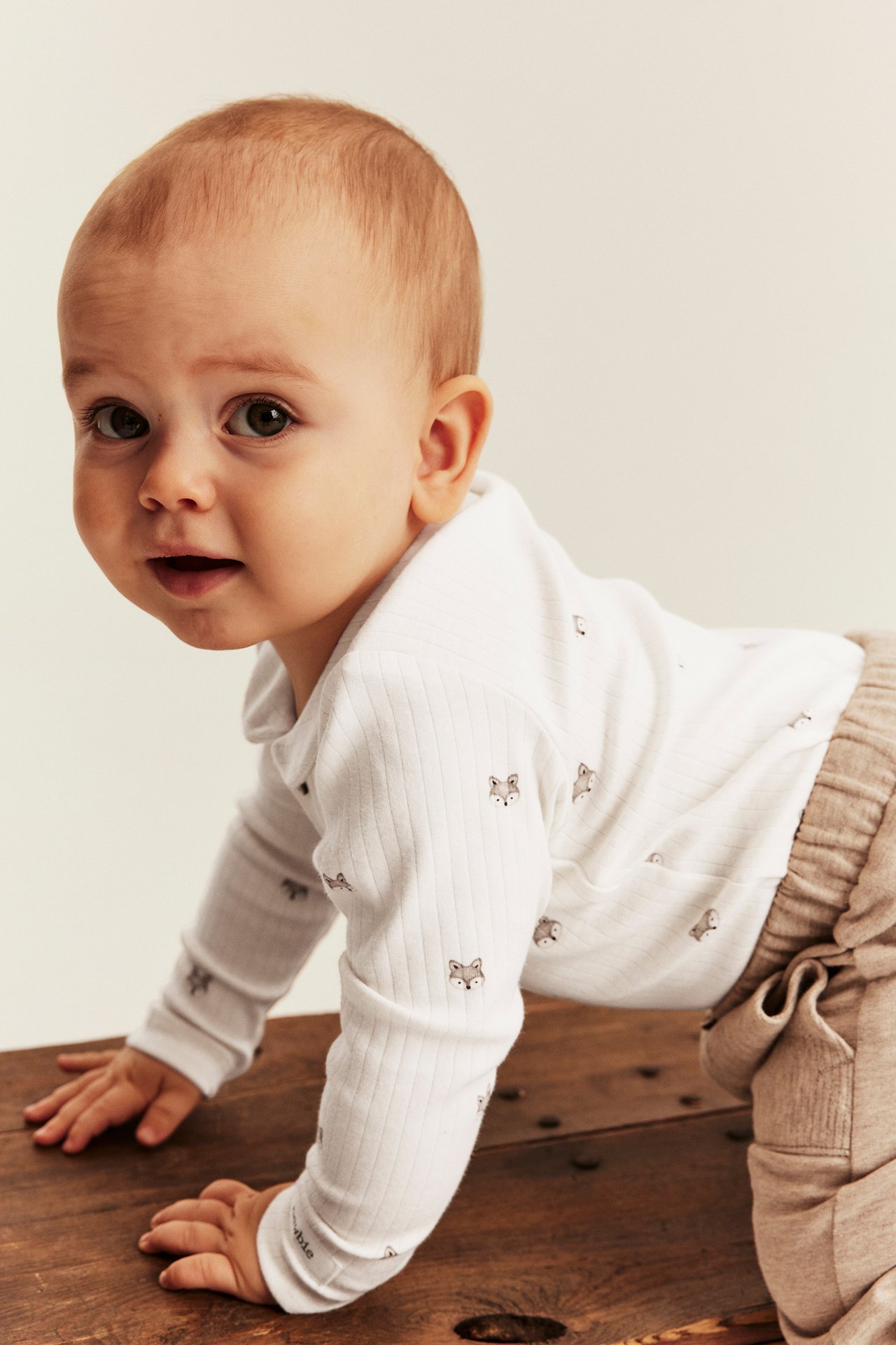 Vorderseitenansicht von Baby in weißem gerippten Langarmshirt mit Fuchsprint und hellbrauner gerippter Hose.