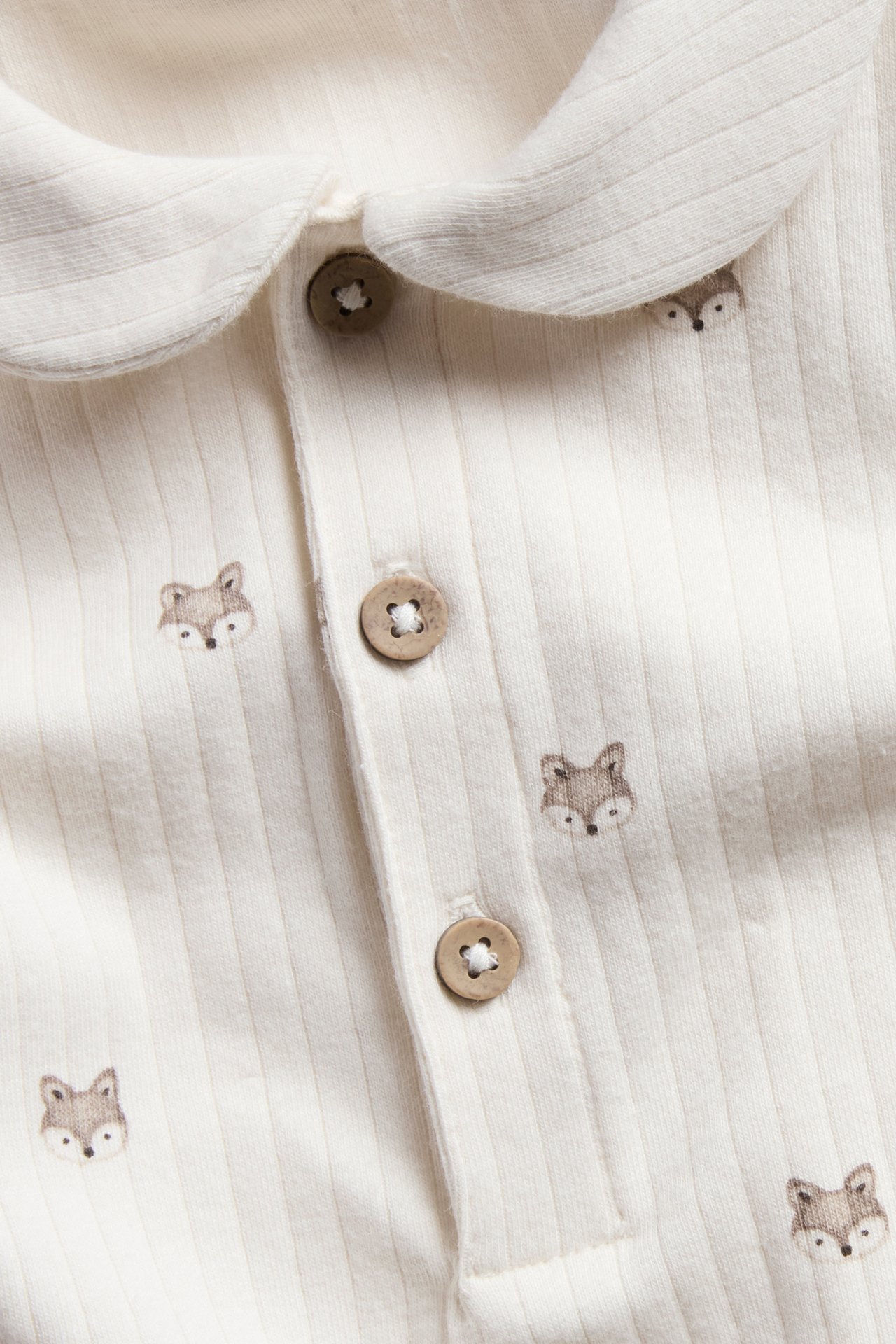 Close-up of a baby's off-white ribbed romper with a Peter Pan collar, fox print, and wooden buttons.