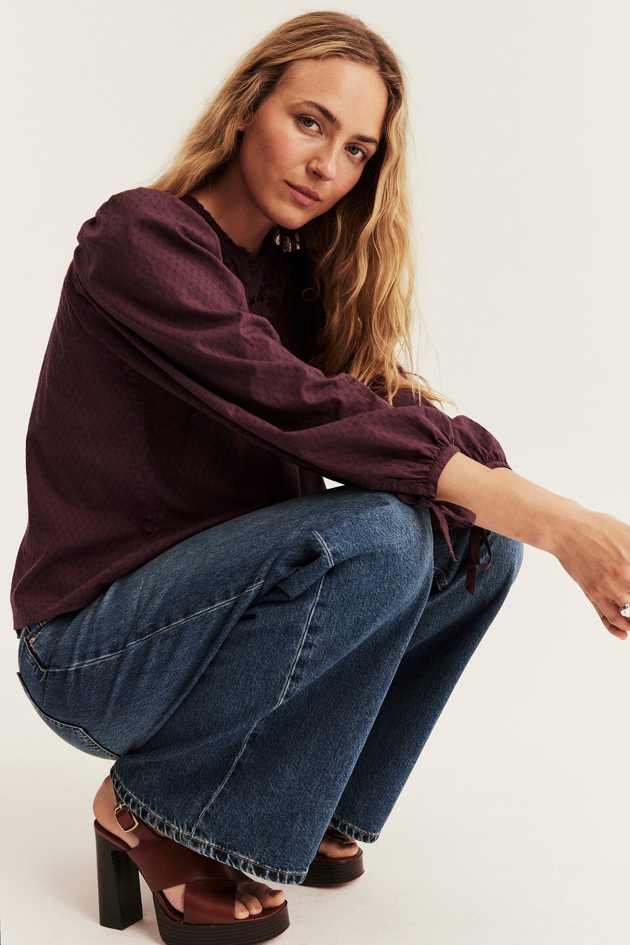 Woman in a dark red patterned blouse, blue jeans, and brown platform sandals, front view.