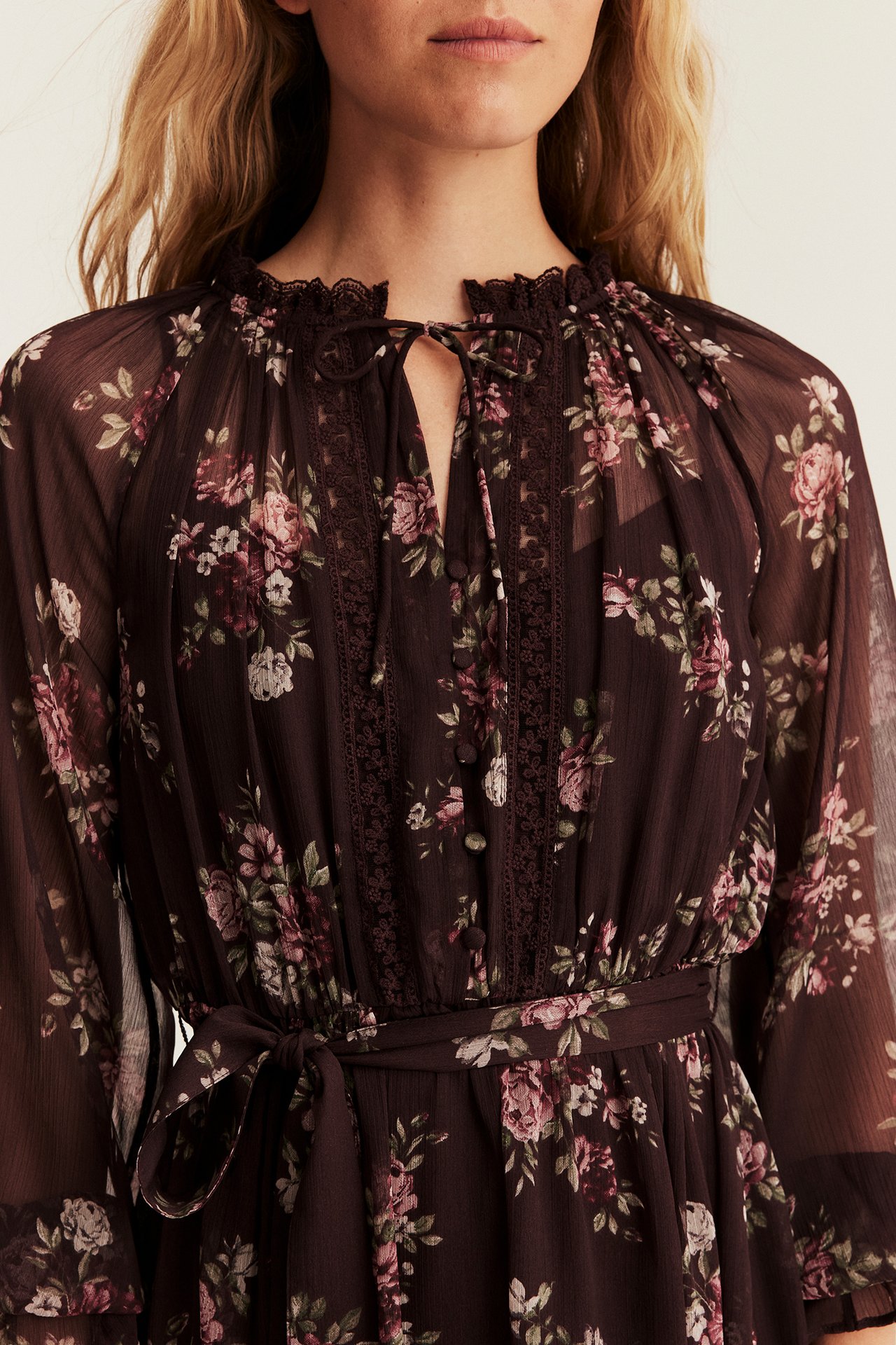 Close-up of a woman wearing a dark floral chiffon dress with a tie neckline and waist belt.