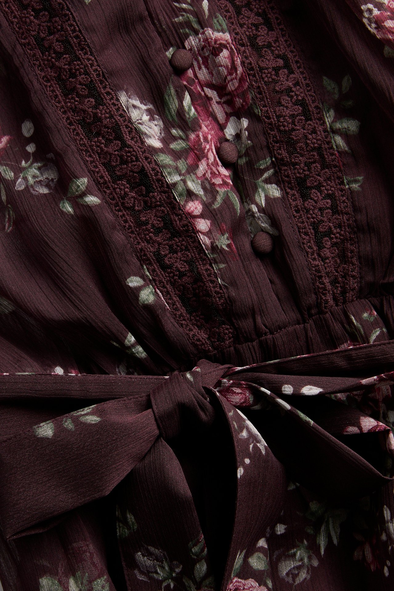 Close-up of a dark red floral dress with lace trim, covered buttons, and a self-tie waist.