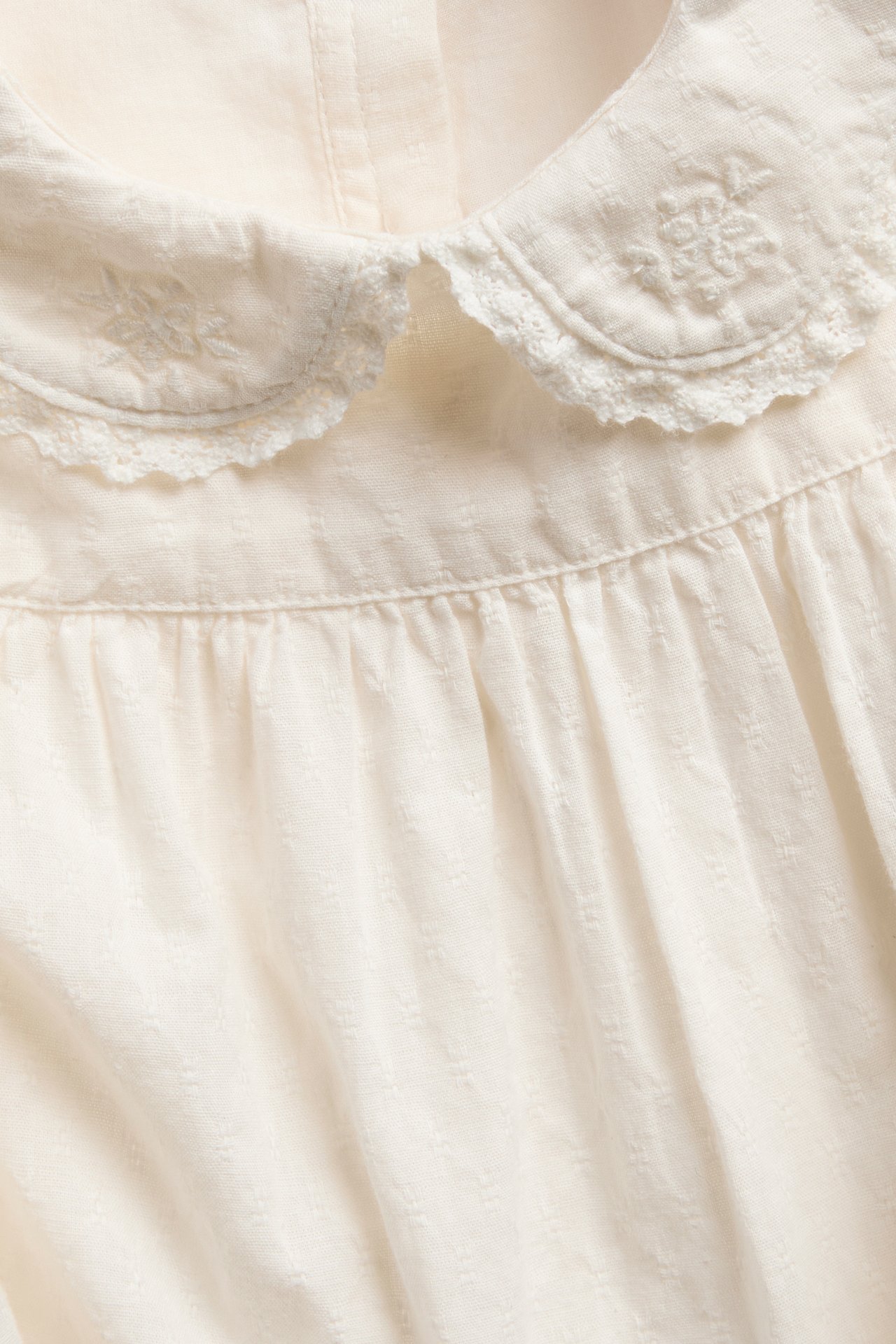 Close-up of an off-white top with an embroidered Peter Pan collar and gathered details.