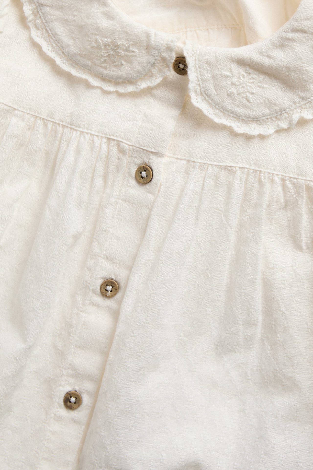 Close-up front view of a cream button-down top with embroidered Peter Pan collar and textured fabric.