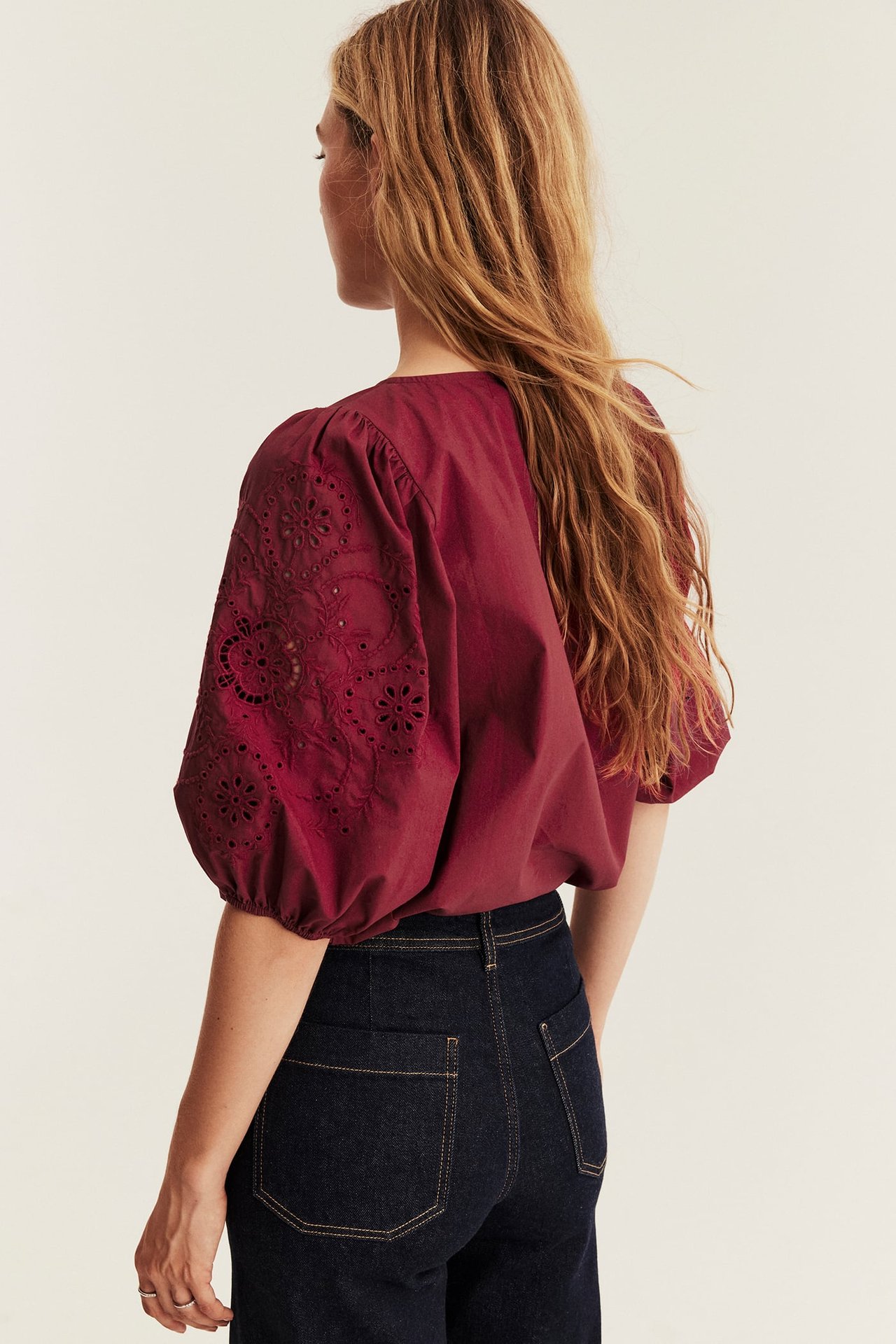 Back view of female model in a maroon puff-sleeve eyelet embroidery top and dark blue denim jeans.