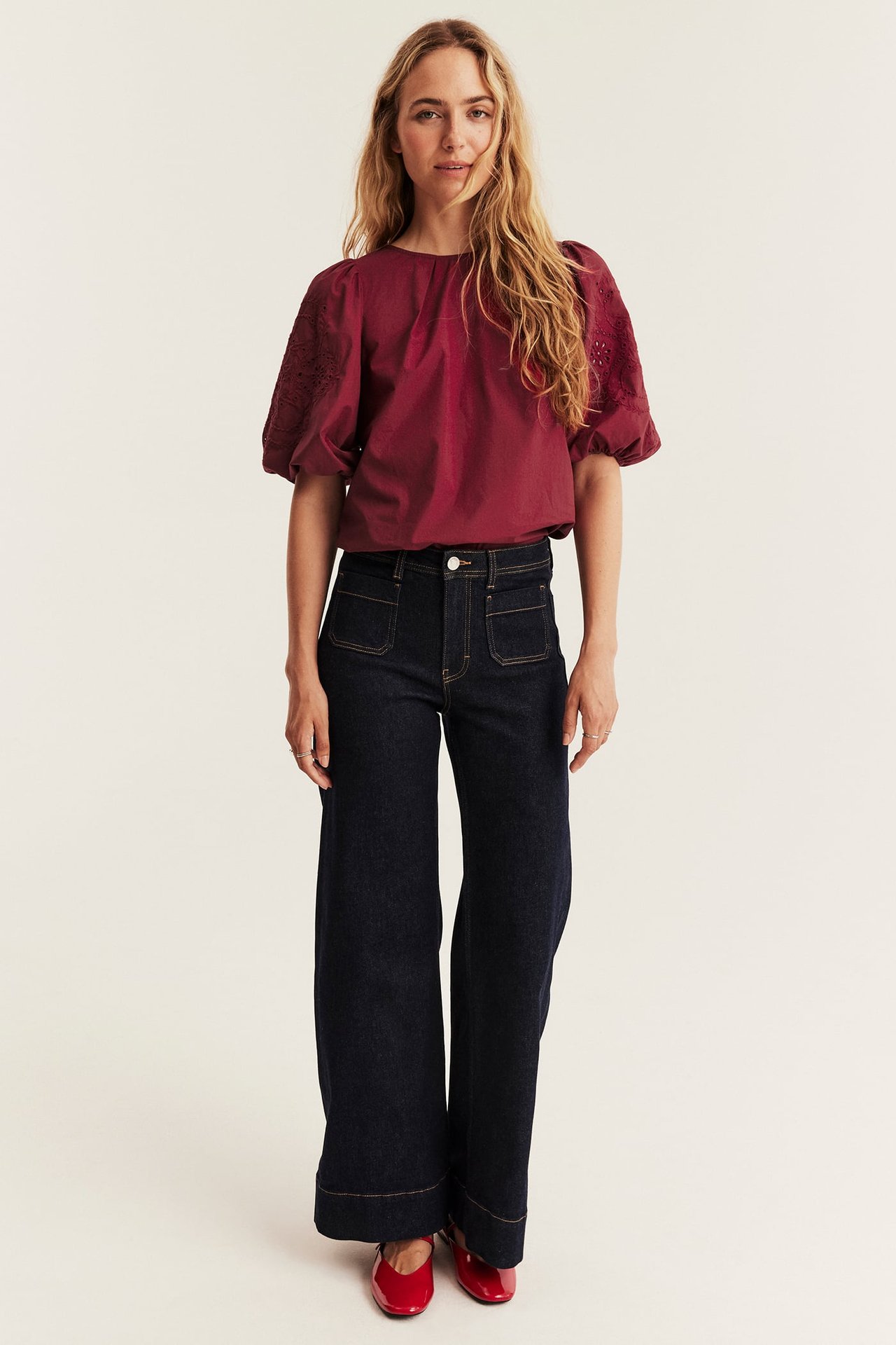 Front view of a woman in dark indigo wide-leg jeans, a maroon puff-sleeve top, and red ballet flats.