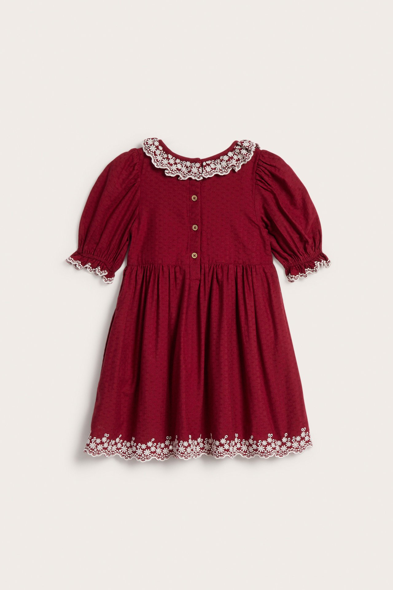 Front view of a kid's red dotted dress with white lace collar, cuffs, and embroidered hem.