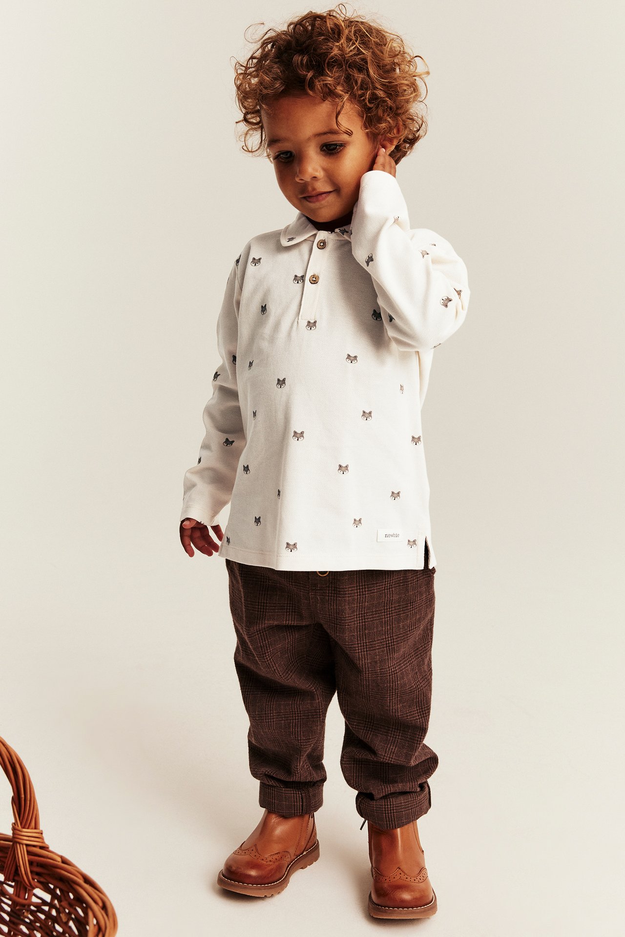 Front view of a kid wearing an off-white long-sleeve polo shirt with fox print, brown plaid pants, and brown wingtip boots.