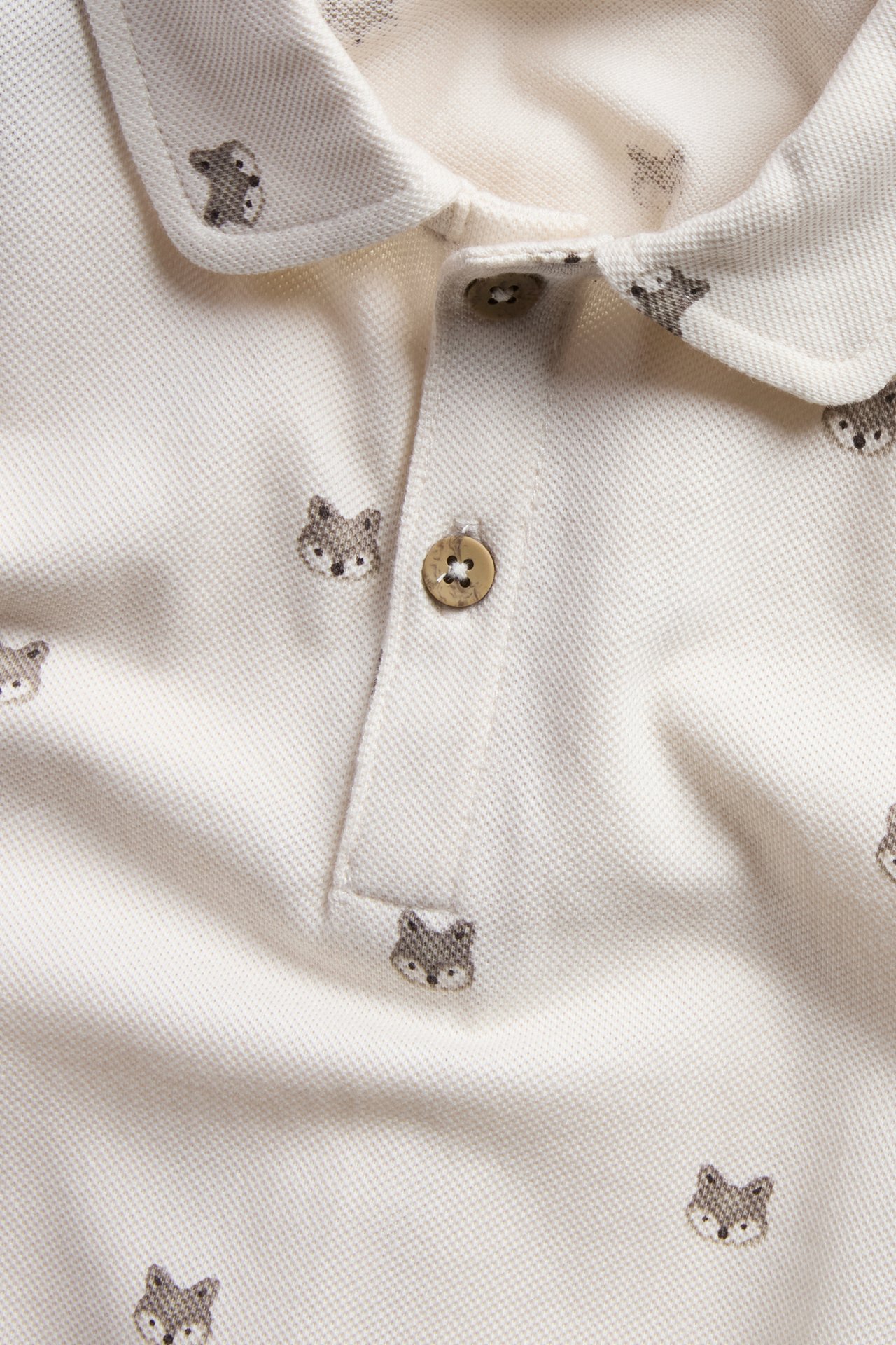 Nahaufnahme eines cremefarbenen Baby-Poloshirts mit Fuchsdruck und zwei Holzknöpfen.