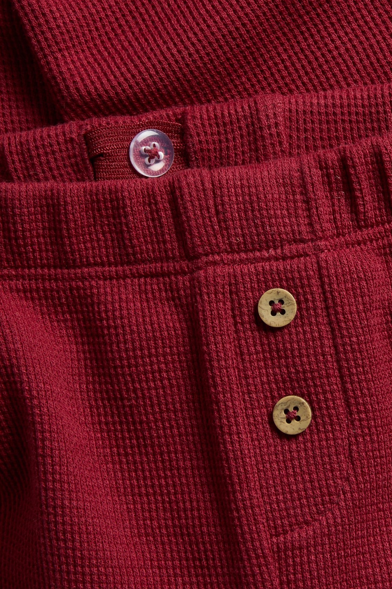 Close-up of a red ribbed pajama garment featuring a clear button and two wooden buttons.