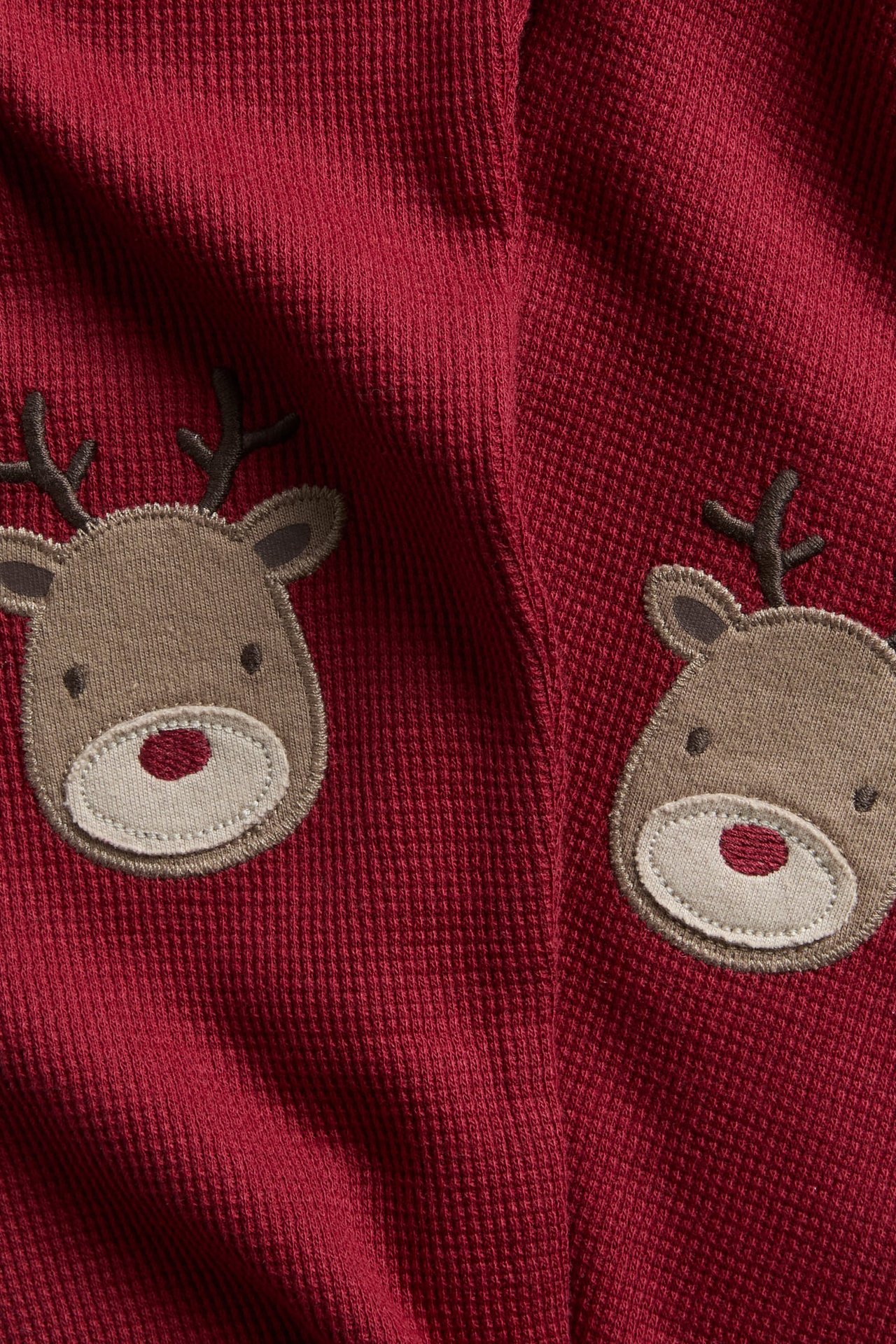 Close-up of a red ribbed fabric with two embroidered brown reindeer faces.