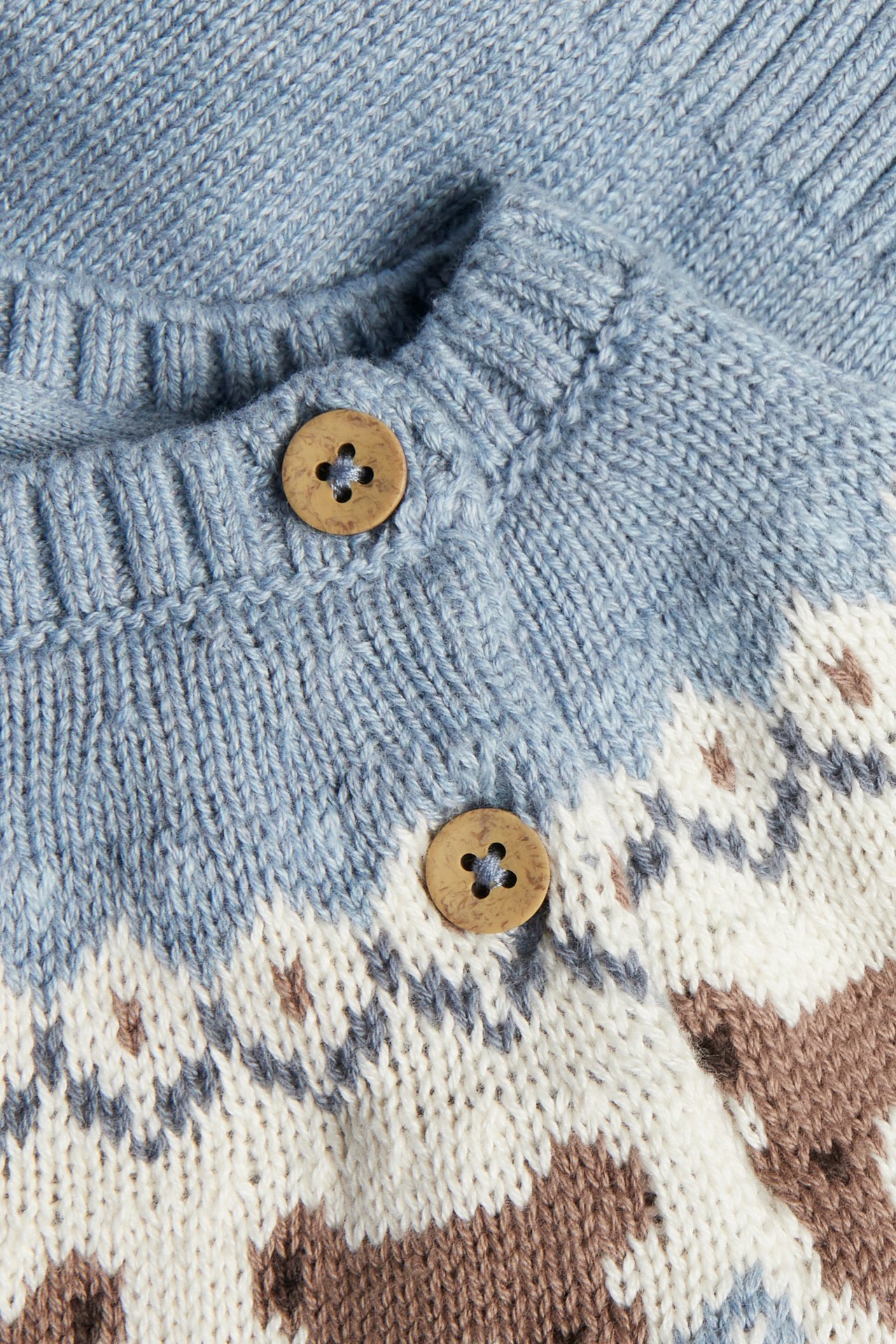 Close-up: light blue knit cardigan with white, gray, brown pattern and two wooden buttons.