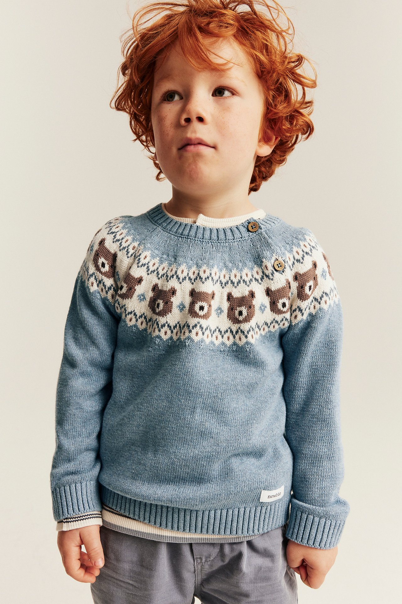 Vorderansicht: Blauer Fair-Isle-Kinderpullover mit Bärenmuster, weißes T-Shirt und graue Hose.