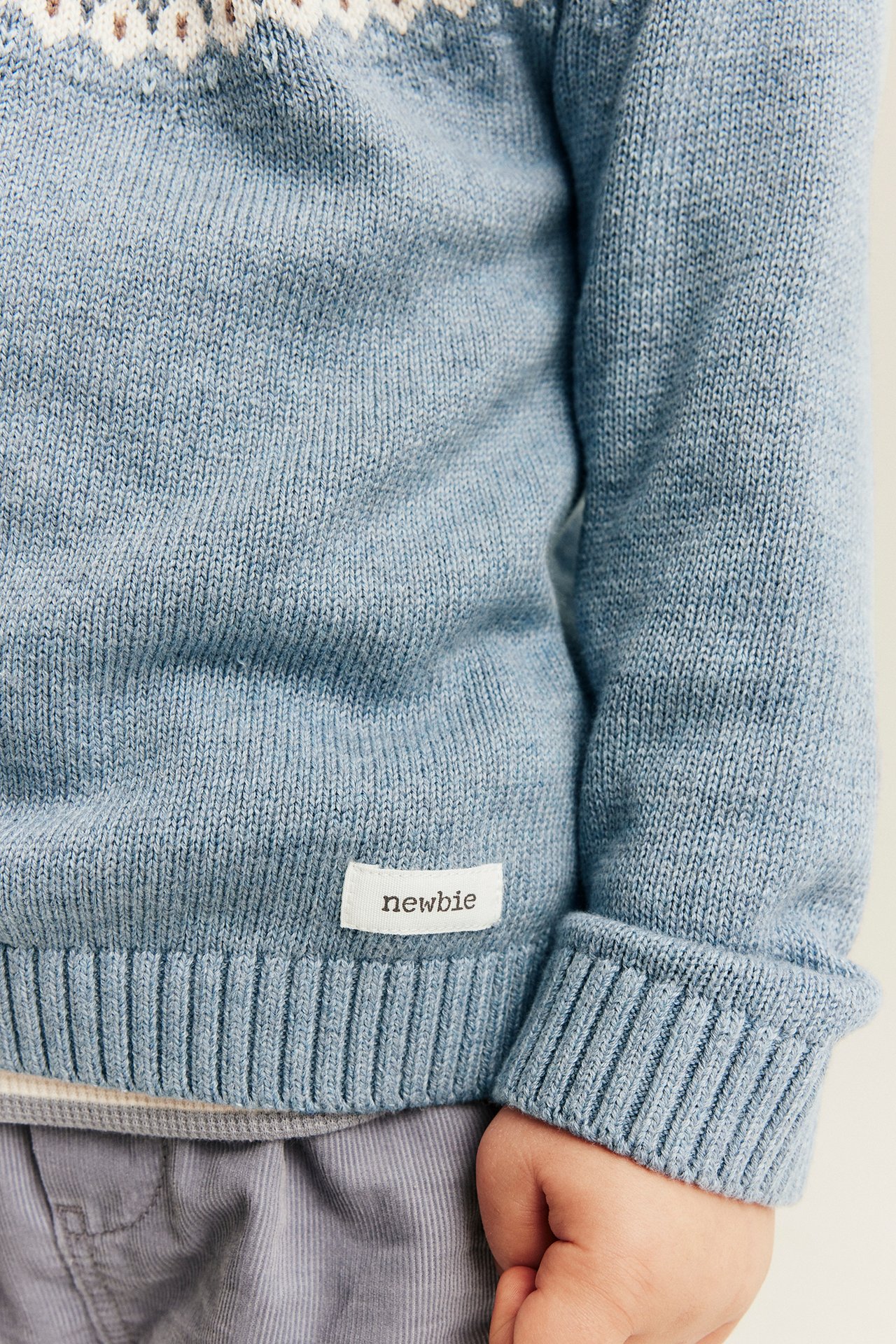 Nahaufnahme eines blauen Kinderstrickpullovers mit Fair-Isle-Muster und grauer Hose.