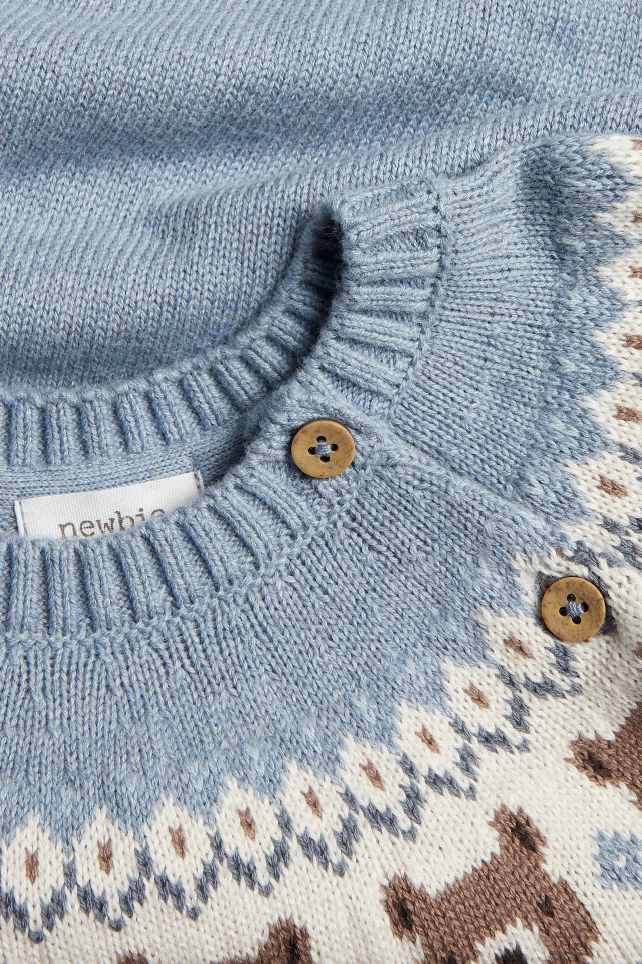 Nahaufnahme einer blauen Baby-Strickjacke mit weißem, braunem Bärenmuster und Holzknöpfen.