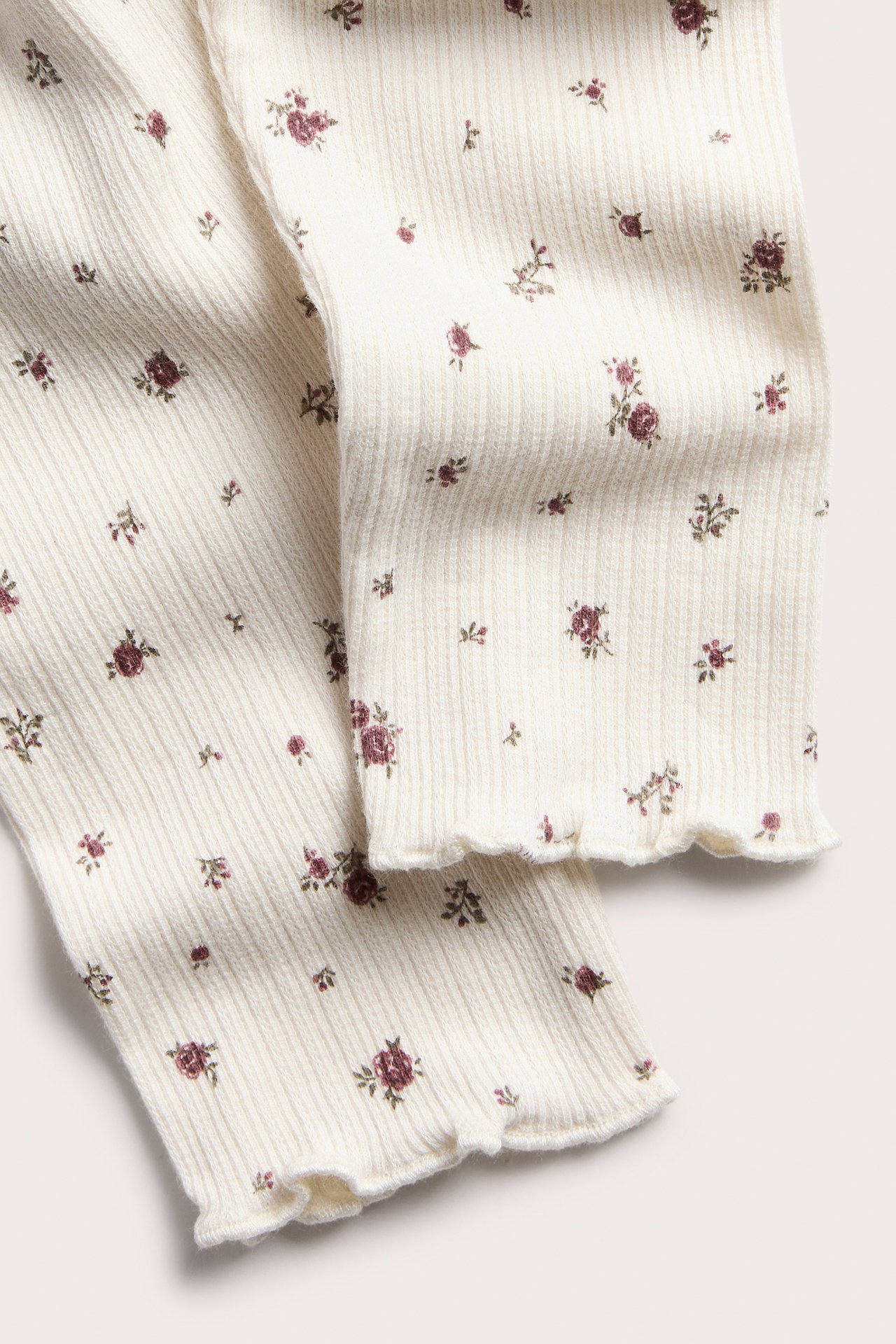 Nahaufnahme von cremefarbenen gerippten Leggings mit Blumenmuster und Rüschensaum.
