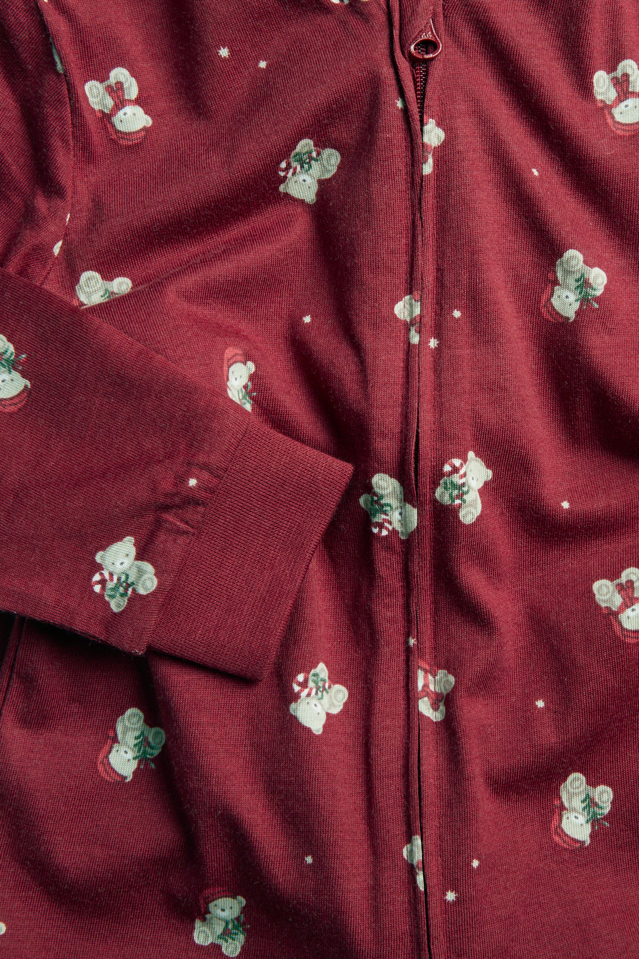 Close-up of a red long-sleeved pajama top with teddy bear and snowflake print and a zipper closure.