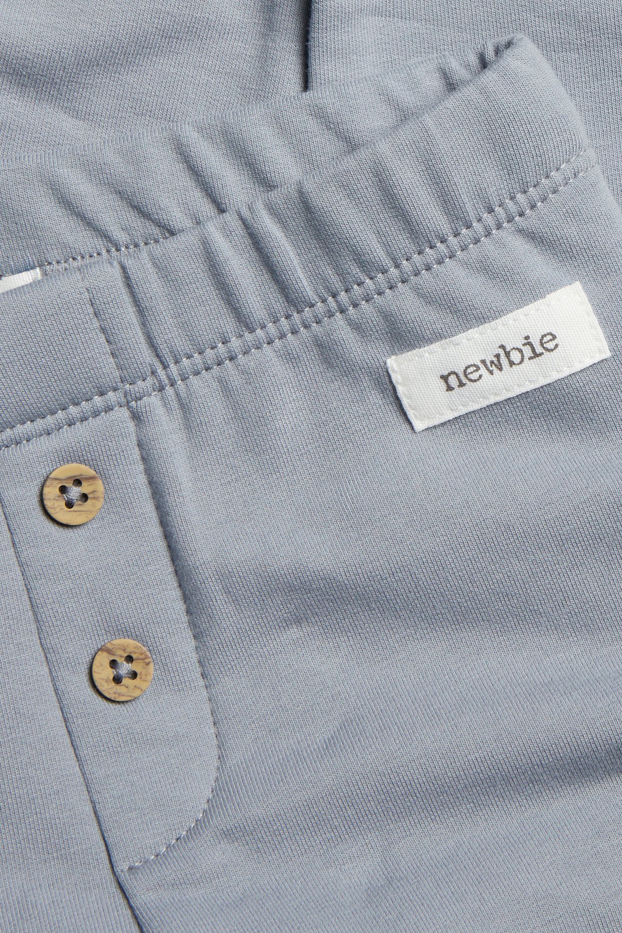 Close-up of baby's light blue jersey pants with elastic waist and decorative wooden buttons.
