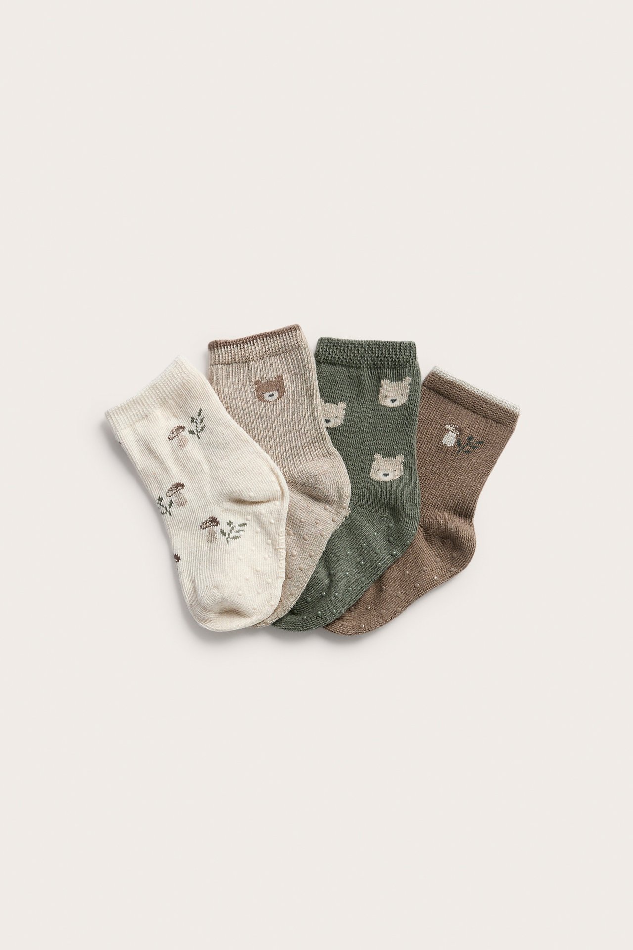 Four pairs of baby non-slip socks: cream, taupe, green, brown with bear and mushroom prints.