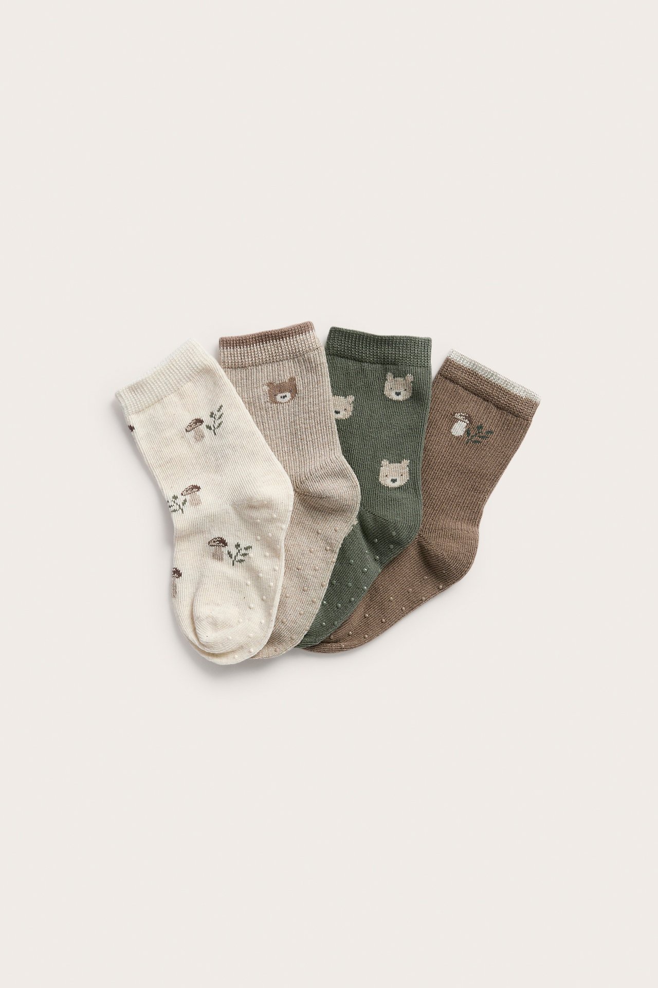 Draufsicht von vier Babysocken: creme mit Pilzen, beige mit Bären, grünen Bären, braunen Pilzen.