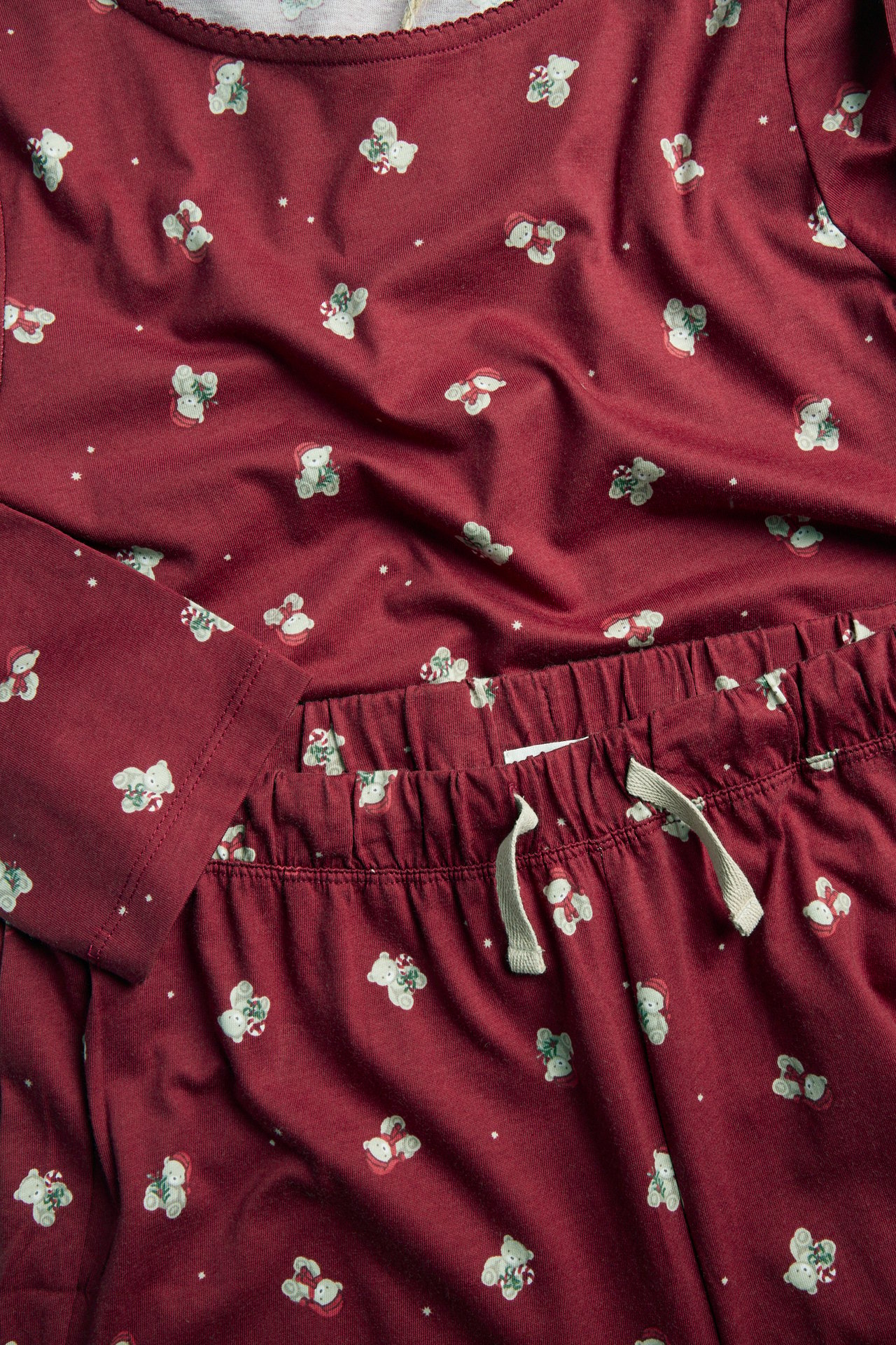 Nahaufnahme eines bordeauxroten Pyjama-Sets mit Weihnachtsbärenmuster und hellgrauem Kordelzug.