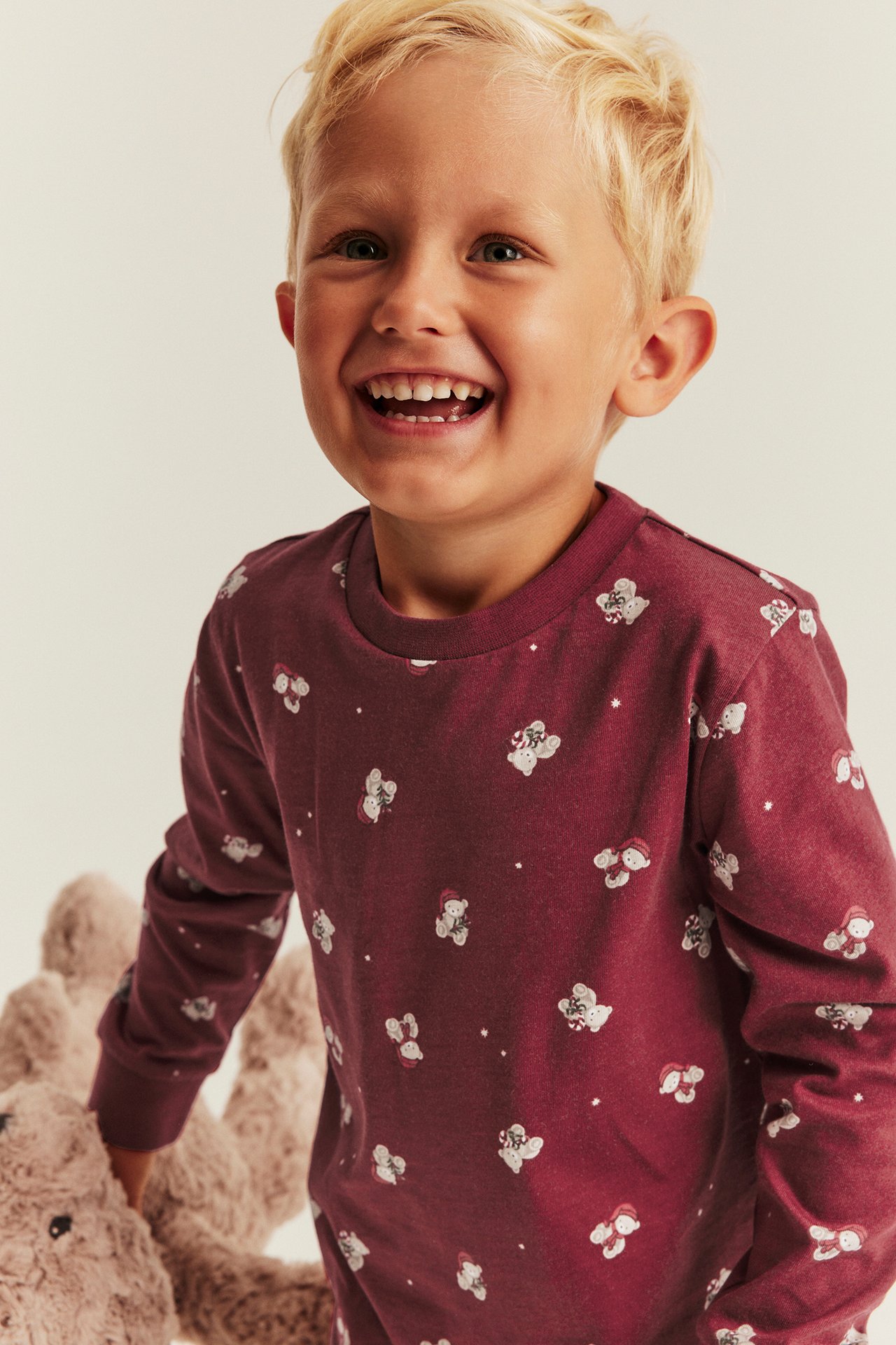Front view of a kid wearing a red long-sleeved top with white teddy bear print, holding a plush toy.