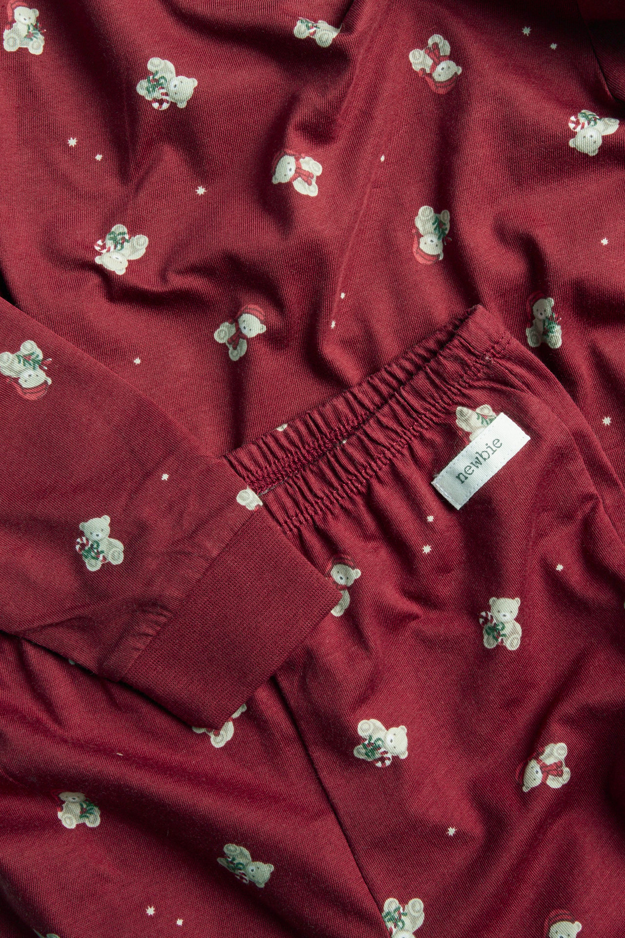 Close-up of baby's maroon pajamas with white teddy bear print and Newbie label.
