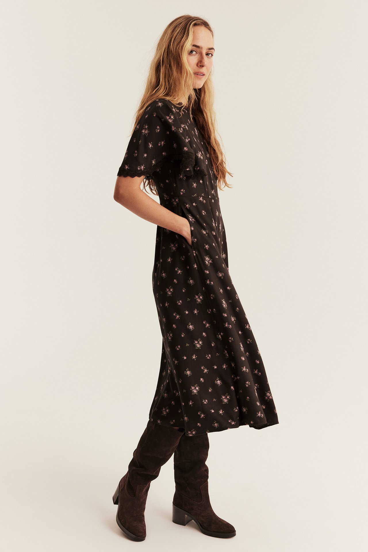 Side view, female model in black floral midi dress with scalloped sleeves and dark brown suede knee boots.