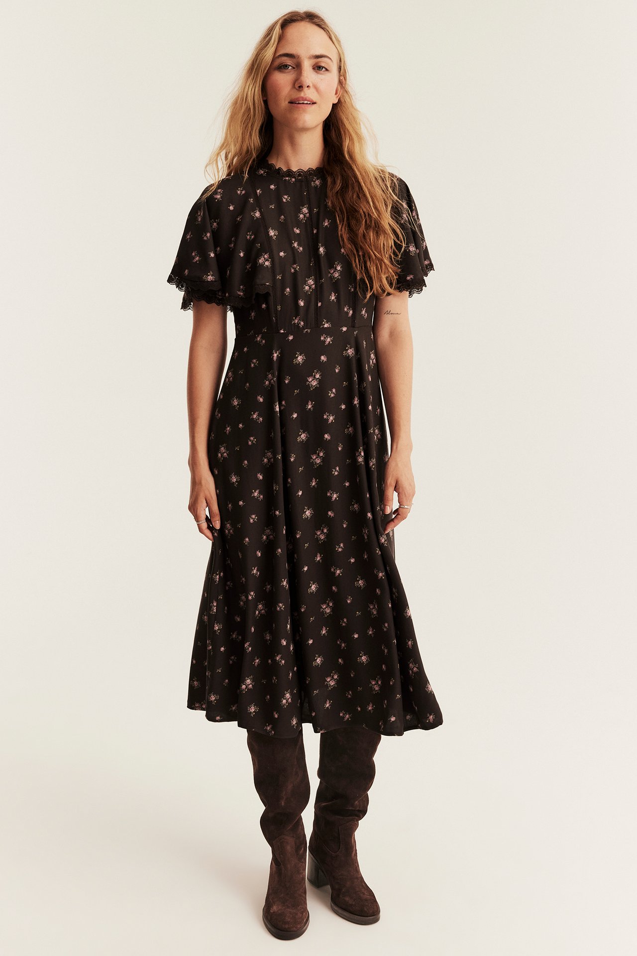 Front view of a woman wearing a black floral midi dress with brown suede knee-high boots.