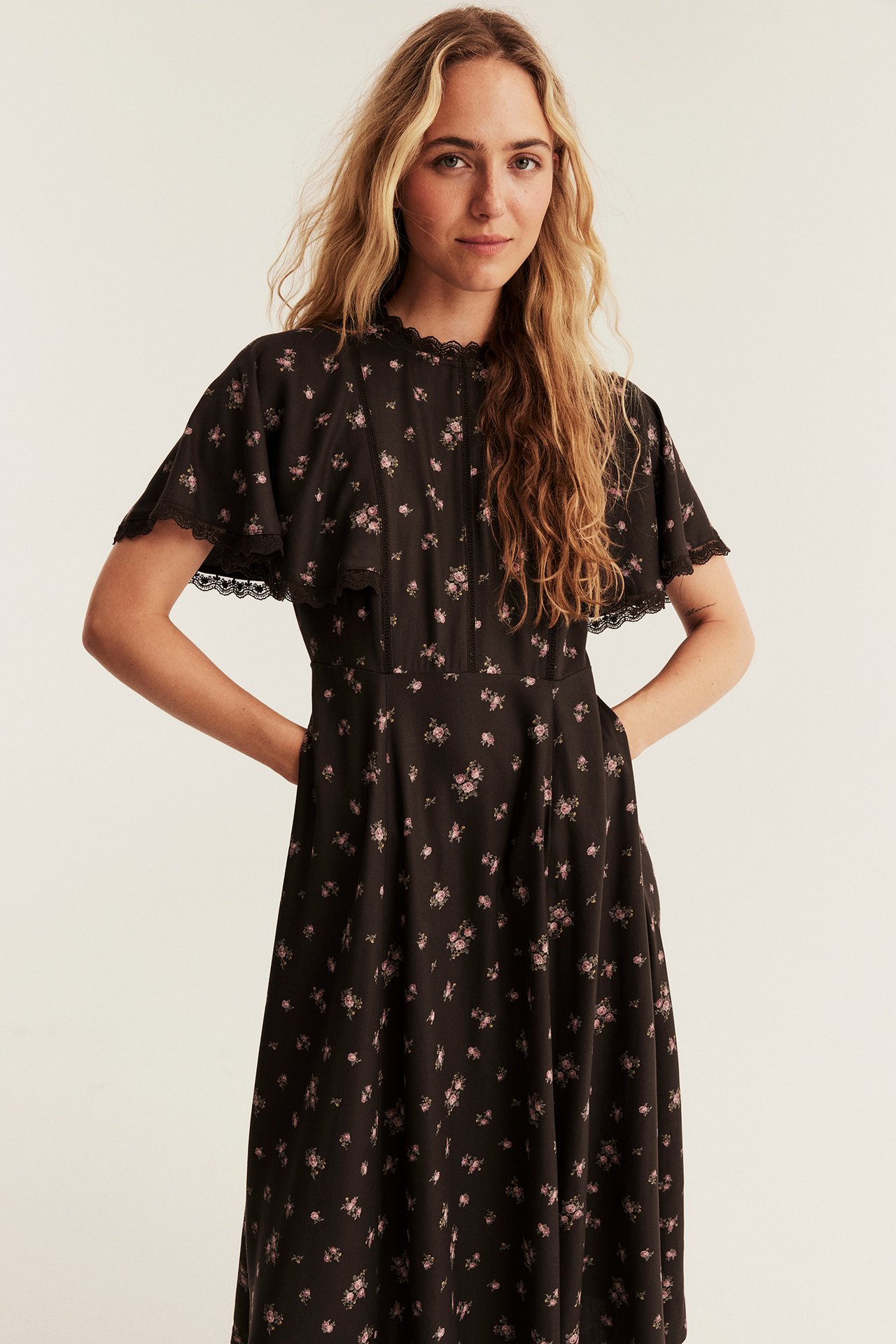 Front view of a woman in a dark brown floral midi dress with small pink roses and lace trim.