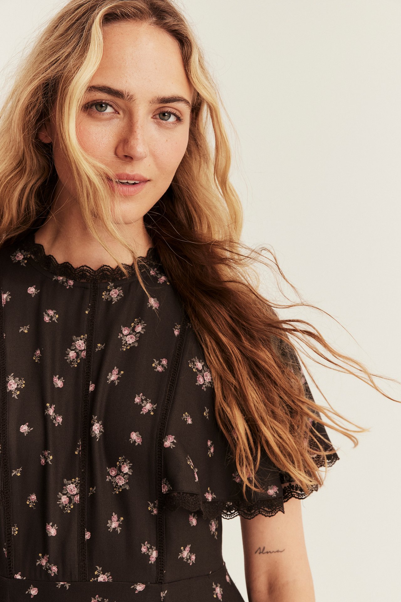 Close-up of female model wearing a black floral short-sleeve dress with pink roses and lace.