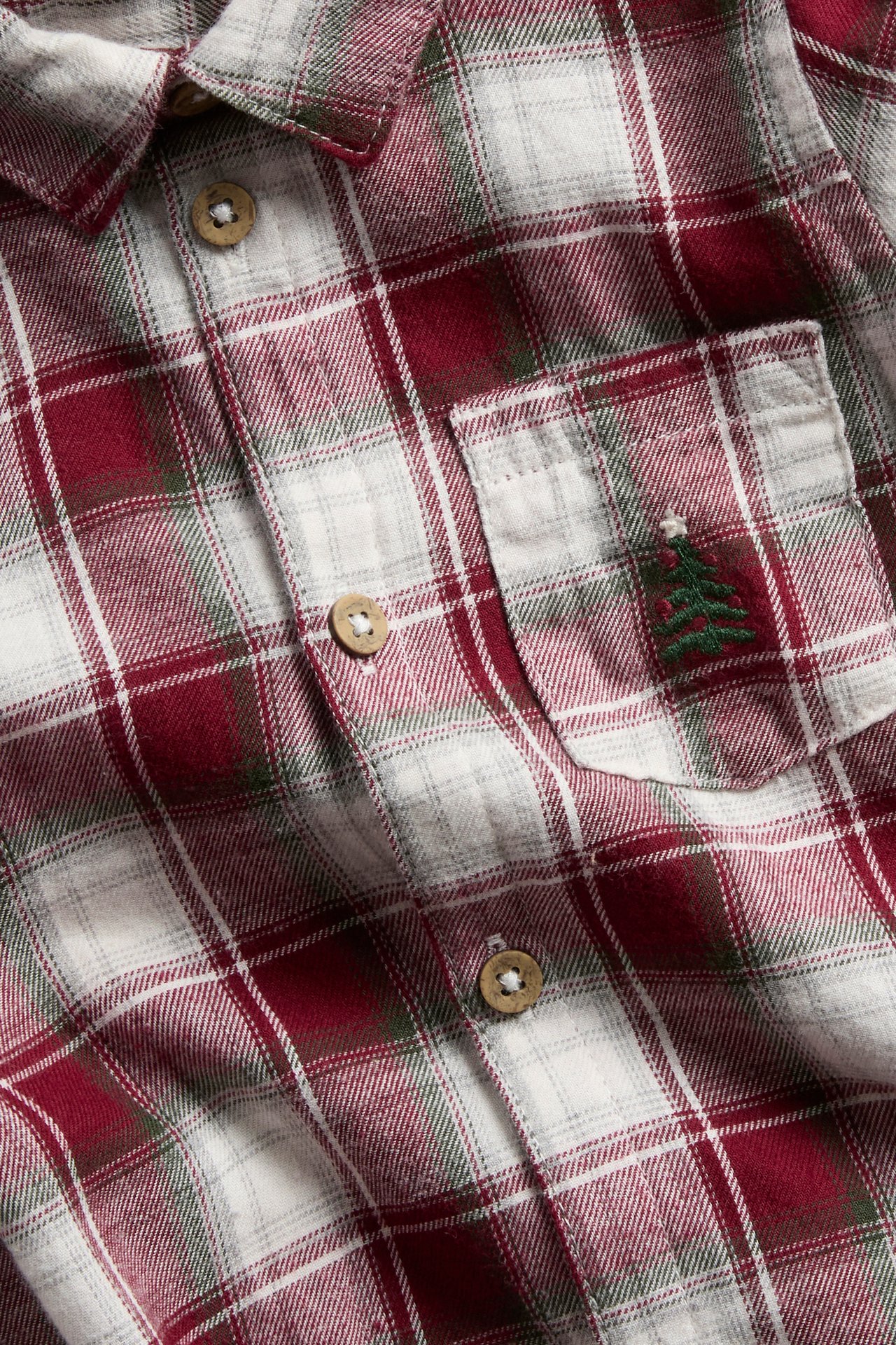 Nahaufnahme eines rot, weiß und grün karierten Flanellhemds mit Weihnachtbaumstickerei auf der Tasche.