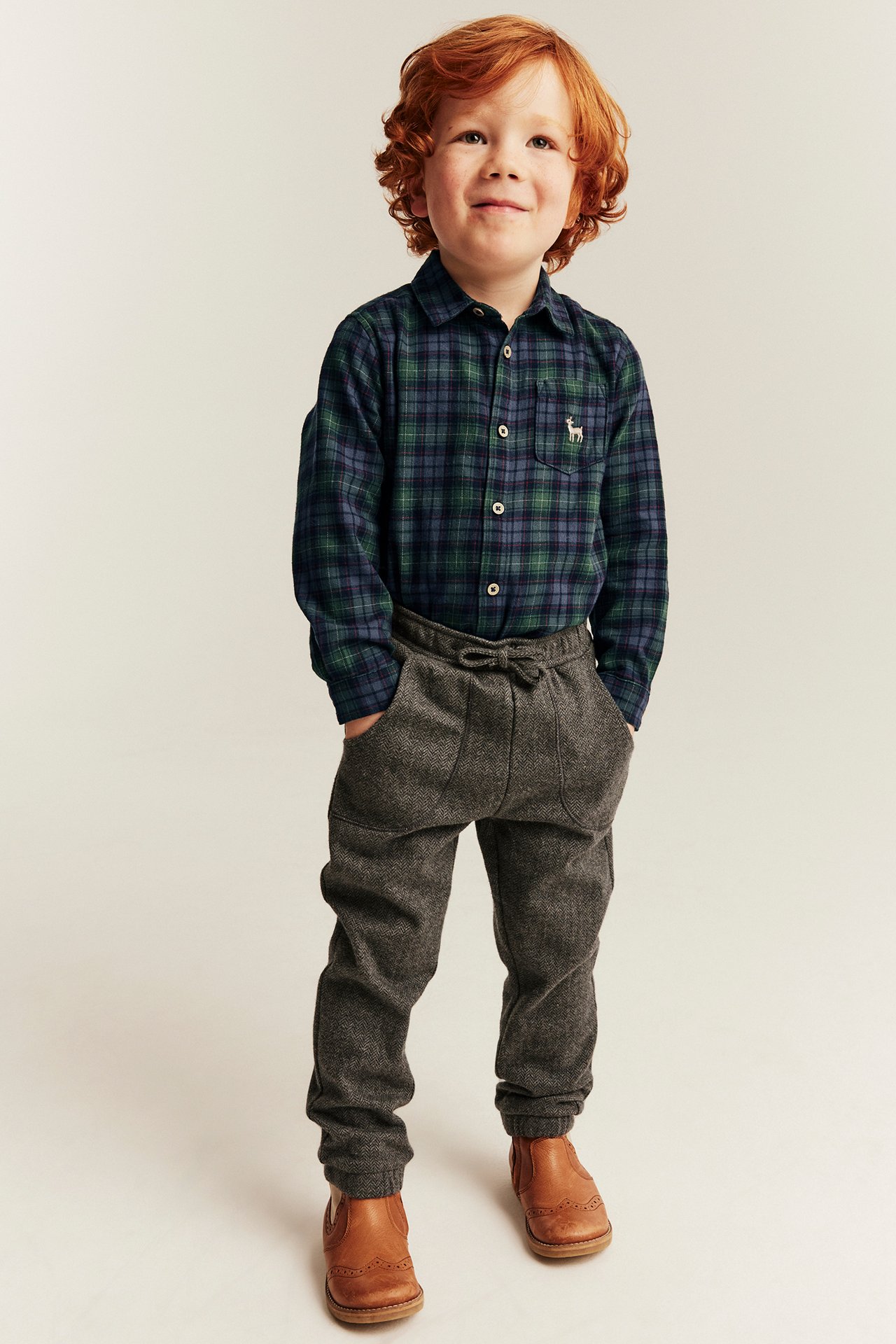 Front view of a kid in a blue-green plaid flannel shirt, gray marled joggers, and brown leather boots.