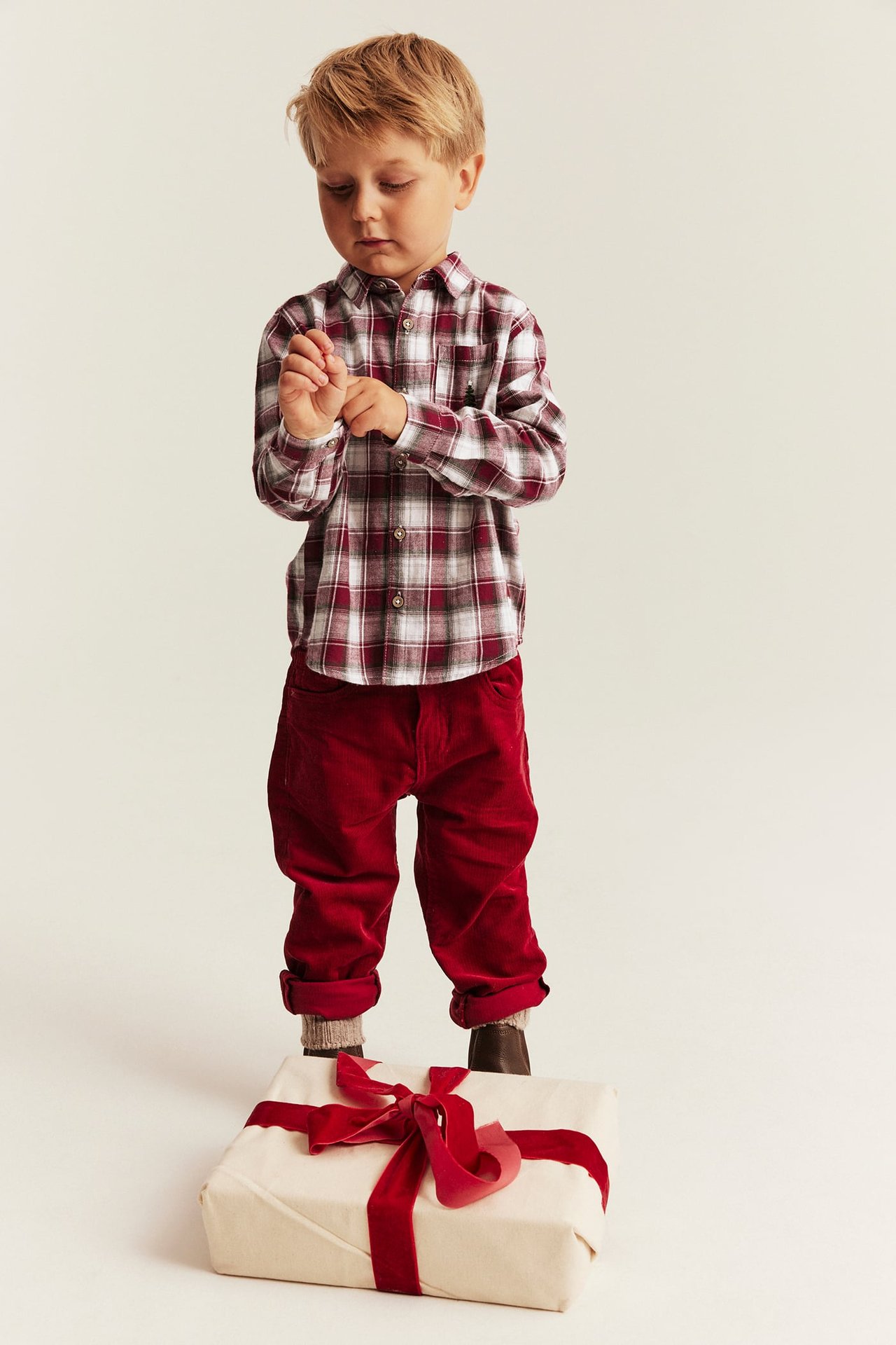 Front view of a kid in a burgundy and white plaid long-sleeve shirt with red corduroy pants.