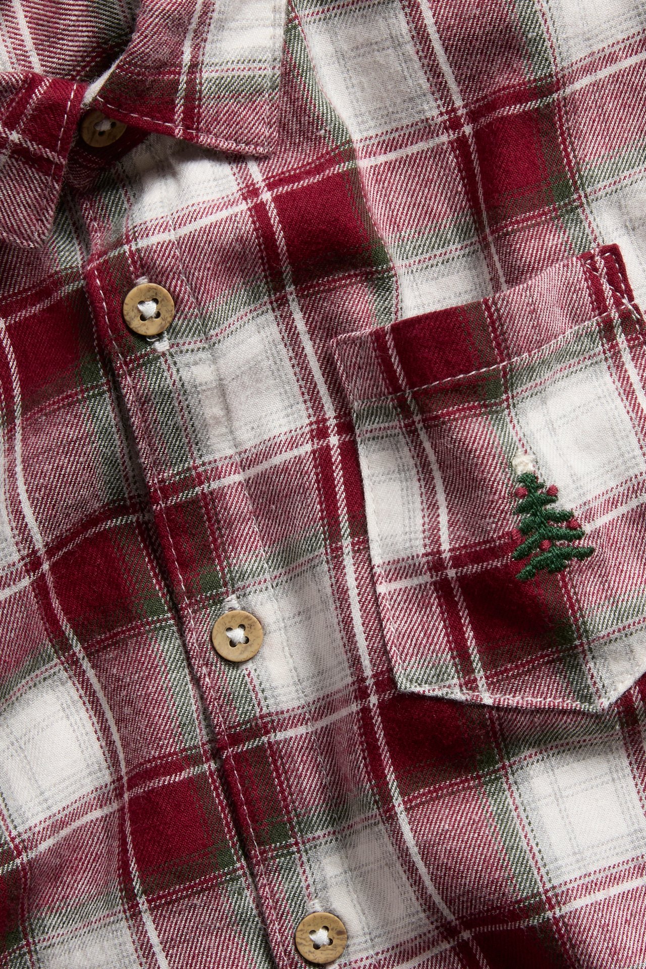 Nahaufnahme eines rot-weiß-grün karierten Flanellhemdes mit Holzknöpfen und besticktem Weihnachtsbaum.
