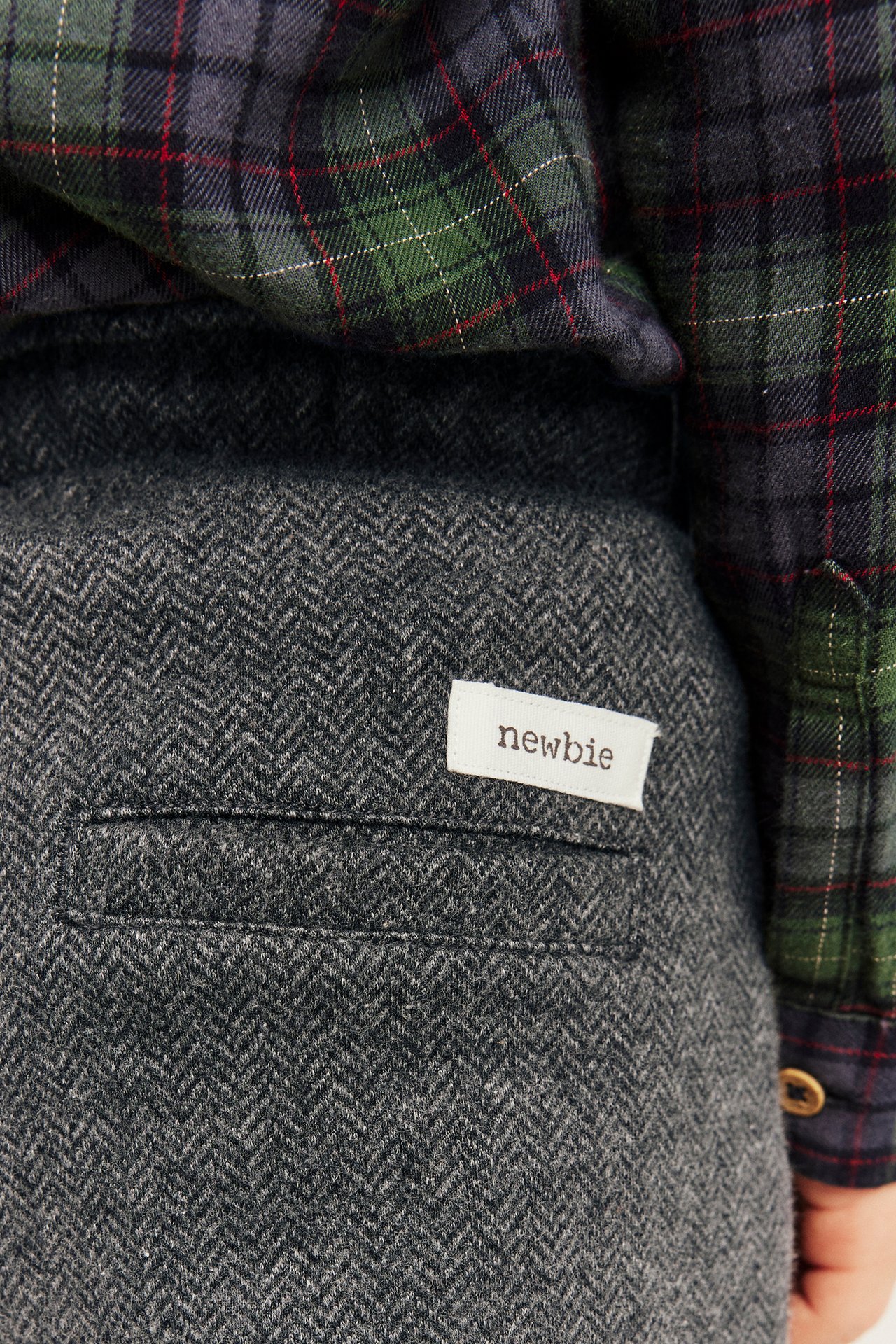 Close-up of dark gray herringbone pants with a 'newbie' label, paired with a green plaid shirt.