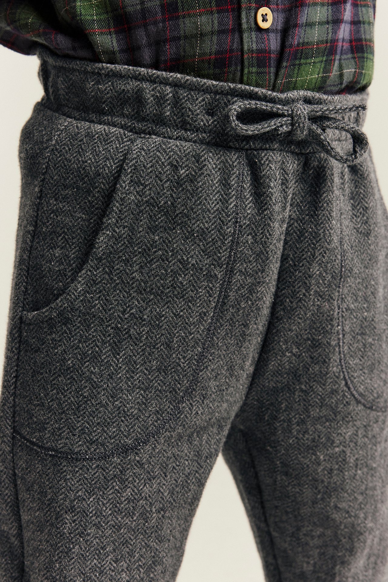 Close-up of gray herringbone drawstring pants with side pockets, worn with a dark green plaid shirt.