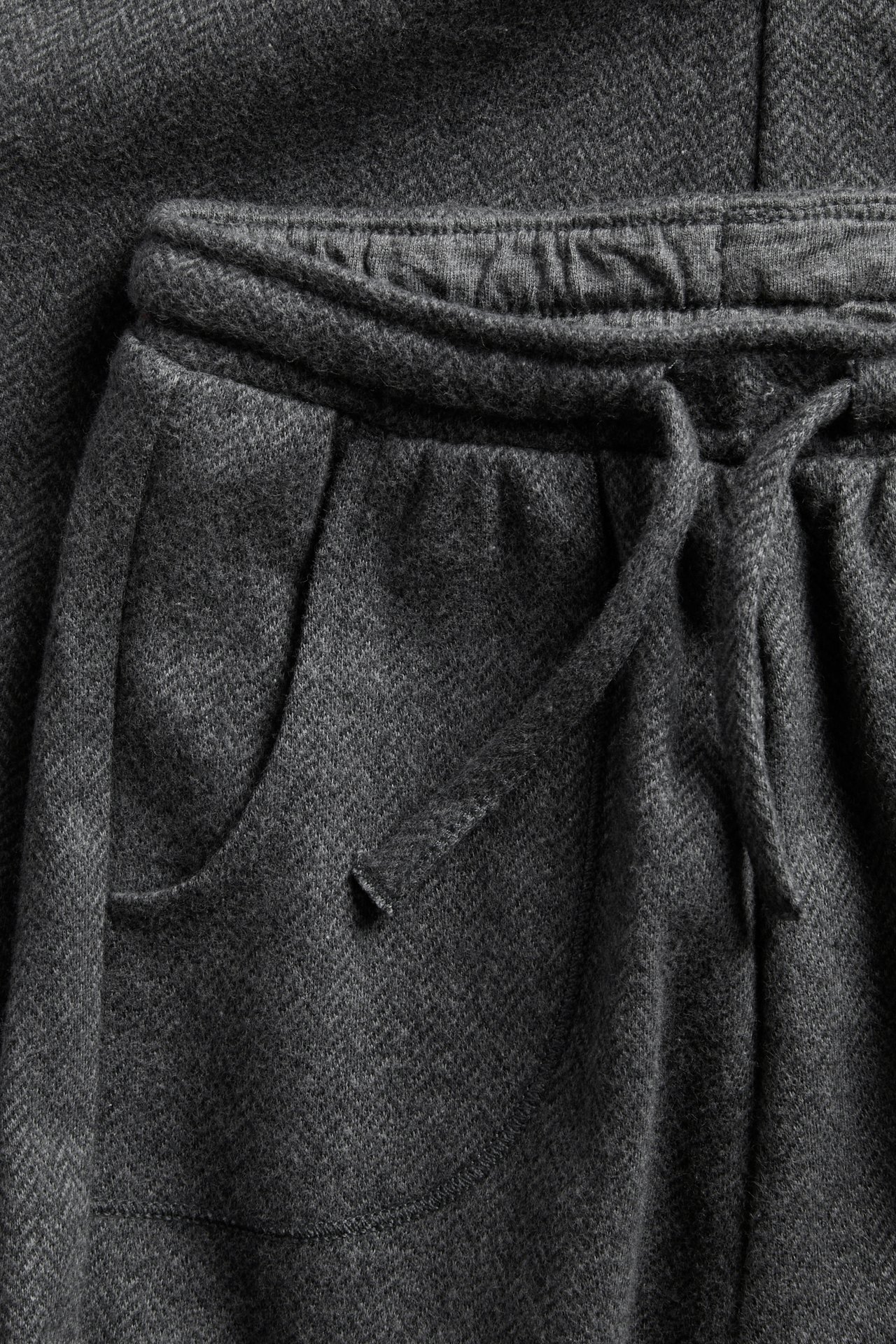 Close-up of dark grey mélange drawstring pants with a pocket, alongside herringbone fabric.