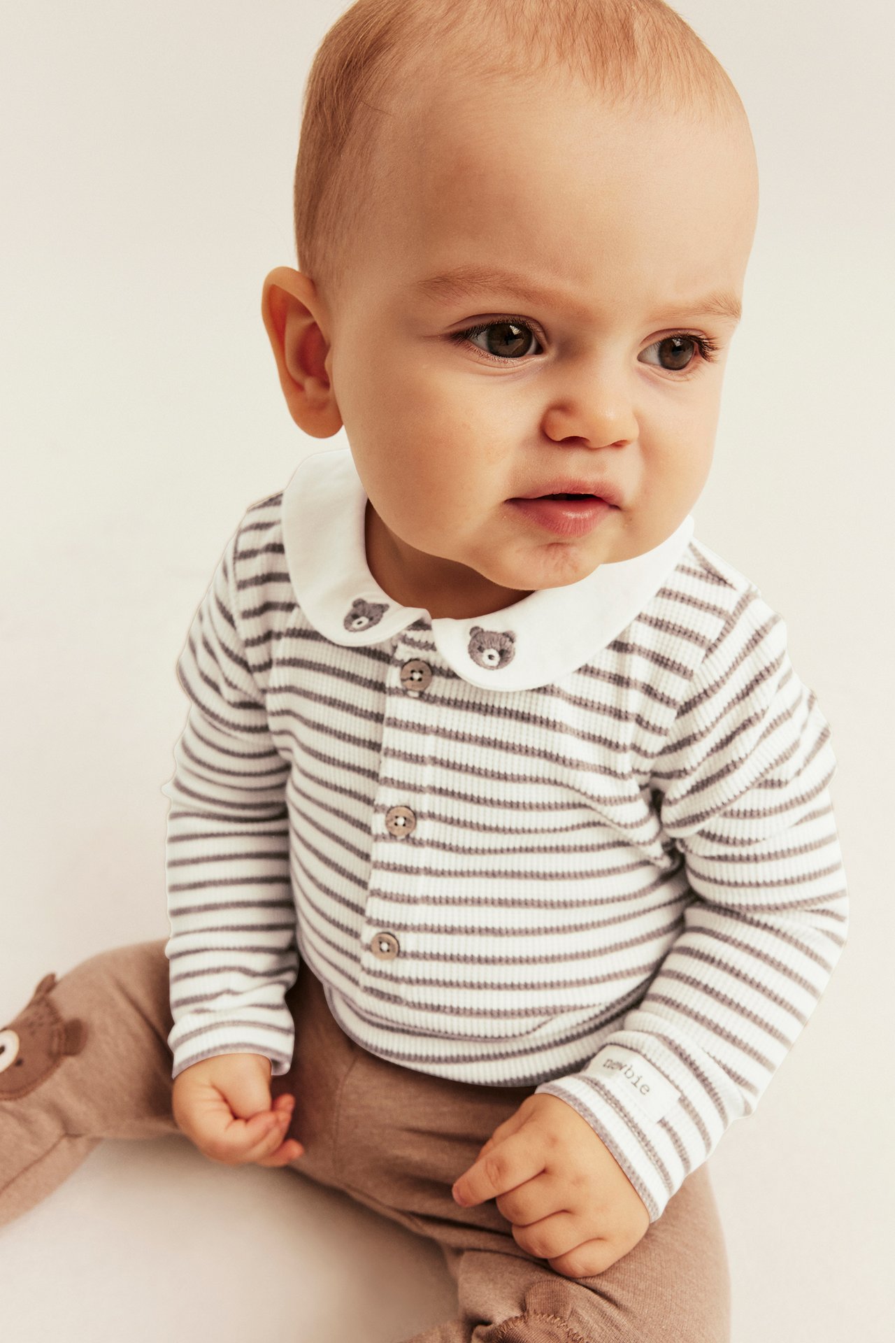 Close-up of baby's white and grey striped ribbed bodysuit with bear collar and brown pants.
