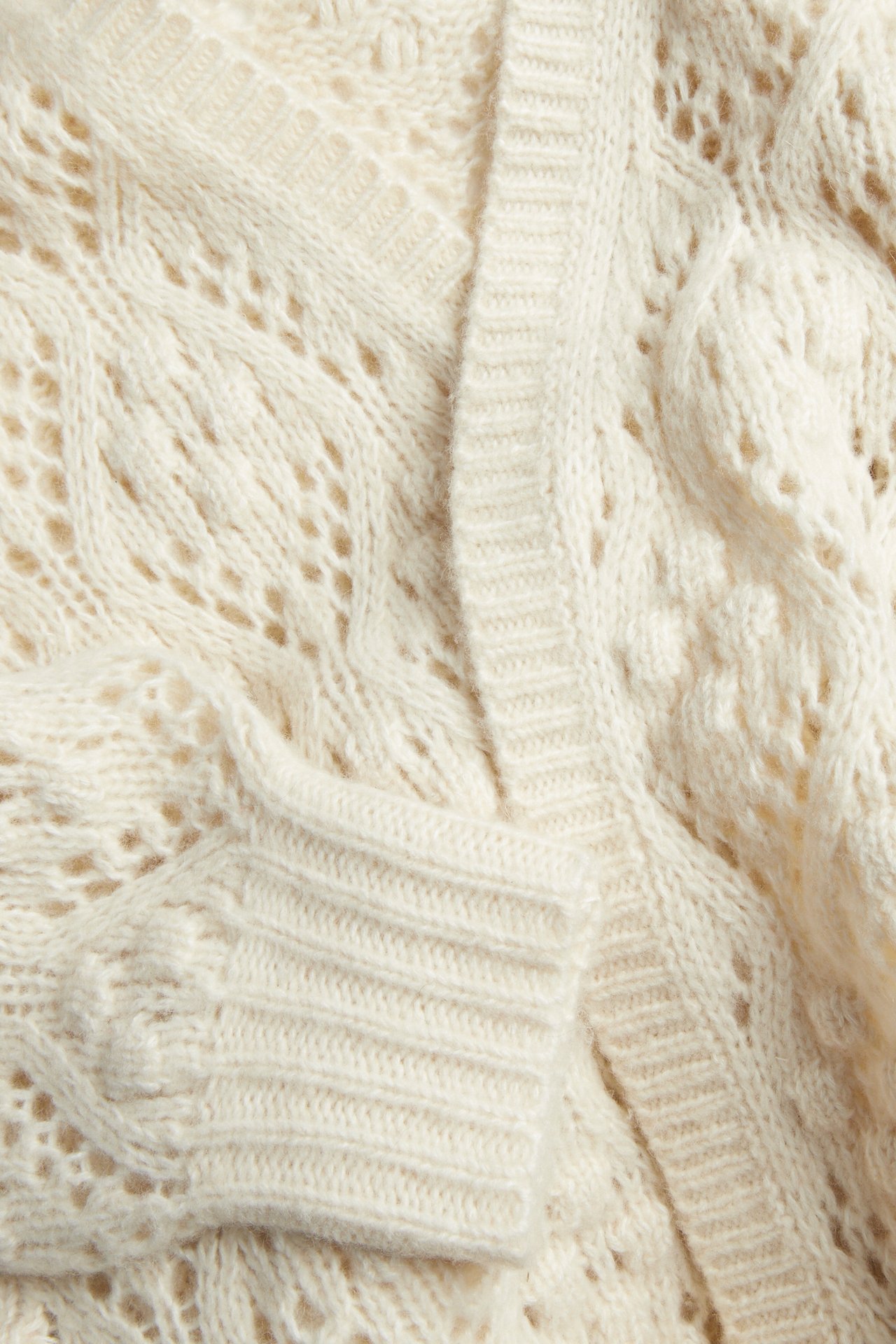 Close-up of a cream cable knit cardigan with openwork details and ribbed edges.