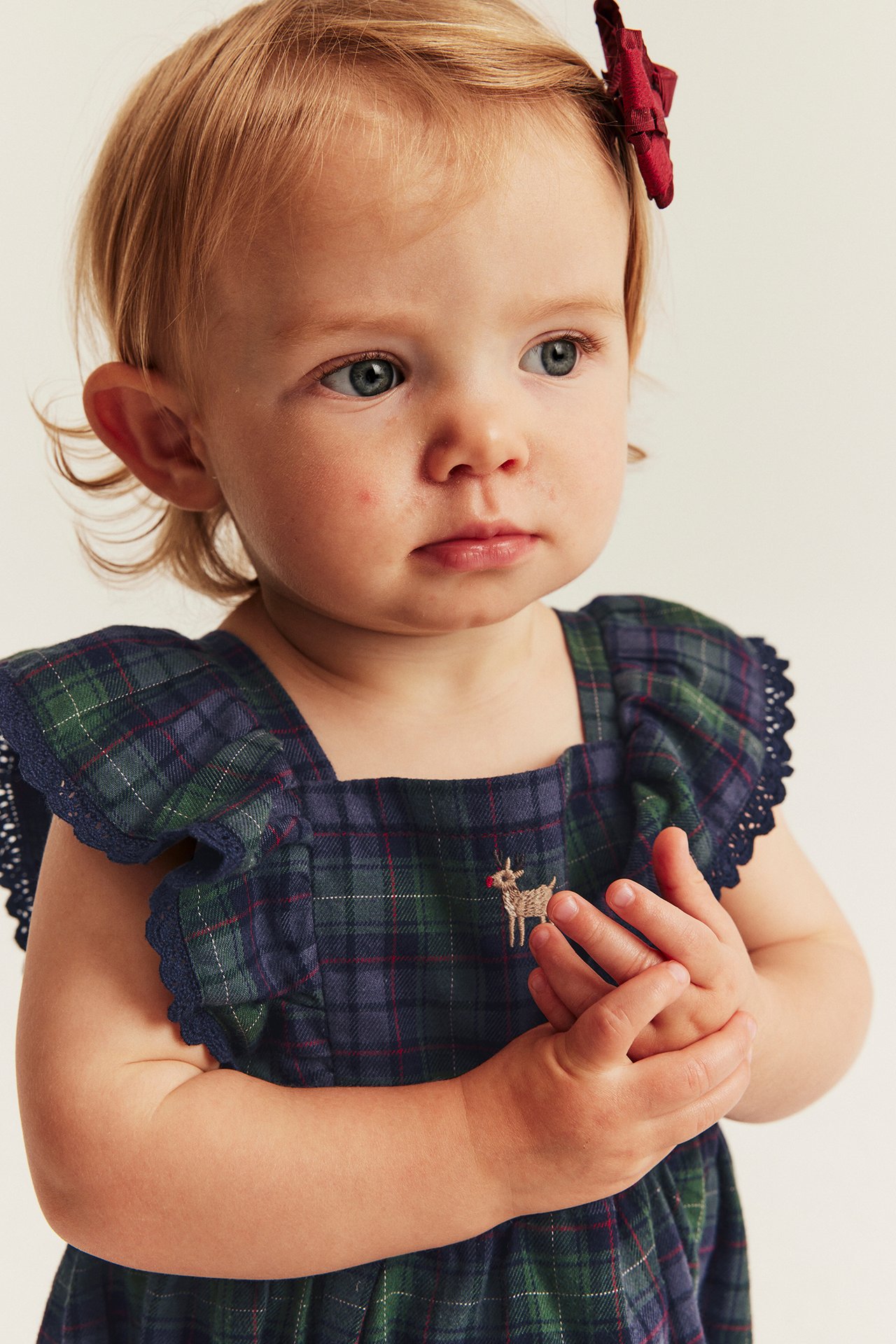 Close-up of a baby in a plaid dress with deer embroidery and a red hair clip.