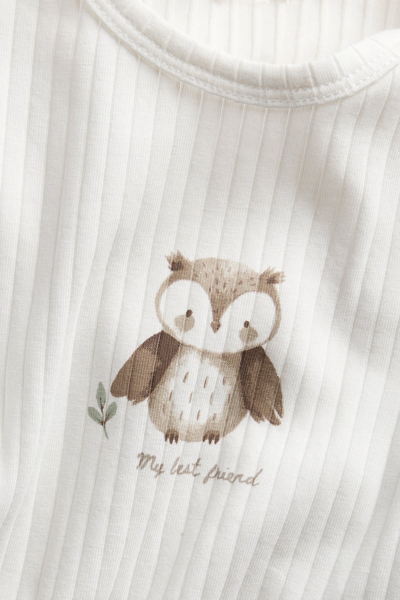 Nahaufnahme eines weißen gerippten Baby-Tops mit braunem Eulendruck und "My best friend" Schriftzug.